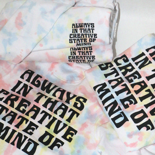 folded tie dye crewneck sweatshirts with text 'Always in that creative state of mind' on a white backdrop
