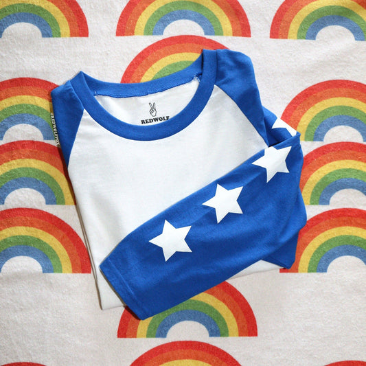 folded shirt with white stars screen printed down the bright blue sleeves of the raglan on a rainbow printed background