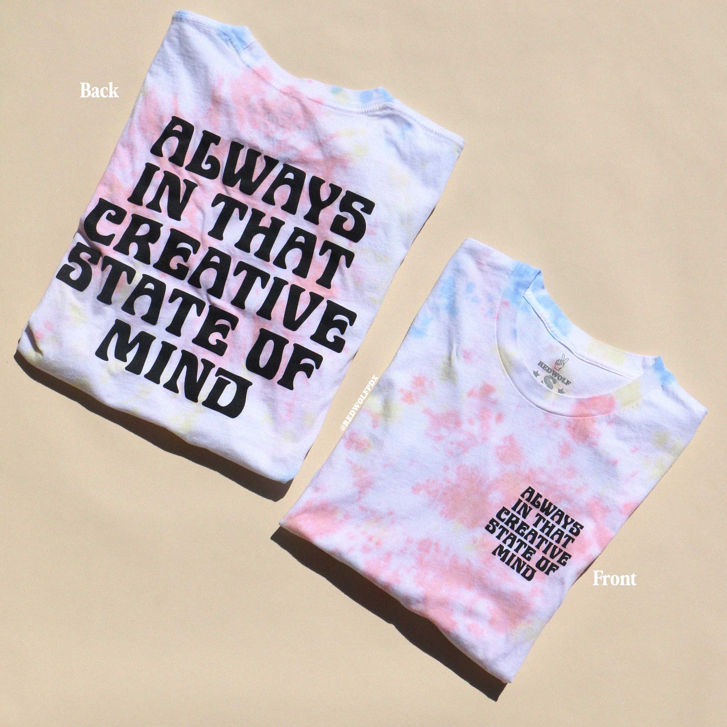 Two tie-dye t-shirts with text 'ALWAYS IN THAT CREATIVE STATE OF MIND' printed on them, one displayed front side up and the other back side up showing the text on the reverse.