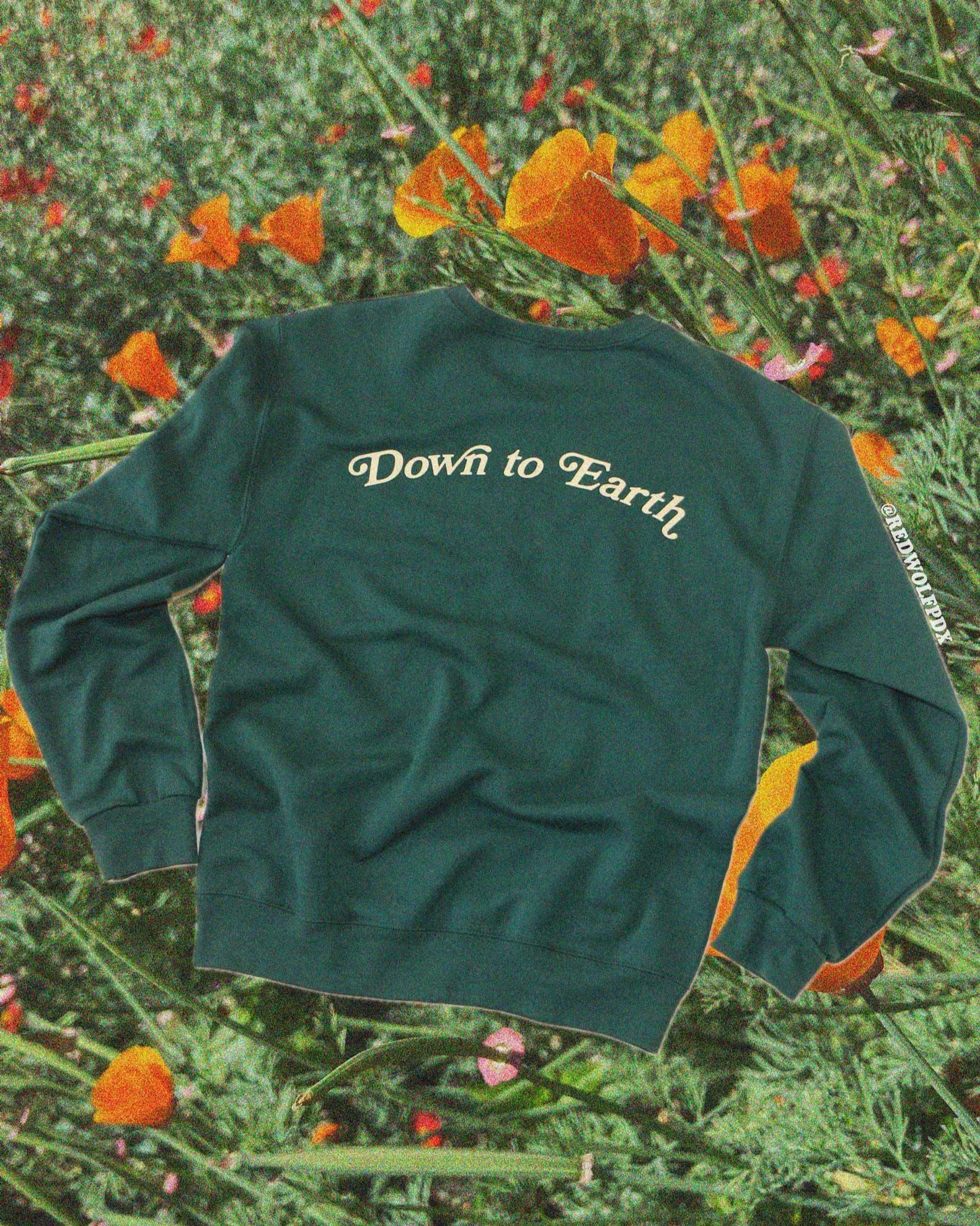 Green sweatshirt with 'Down to Earth' text on a background of greenery and orange flowers