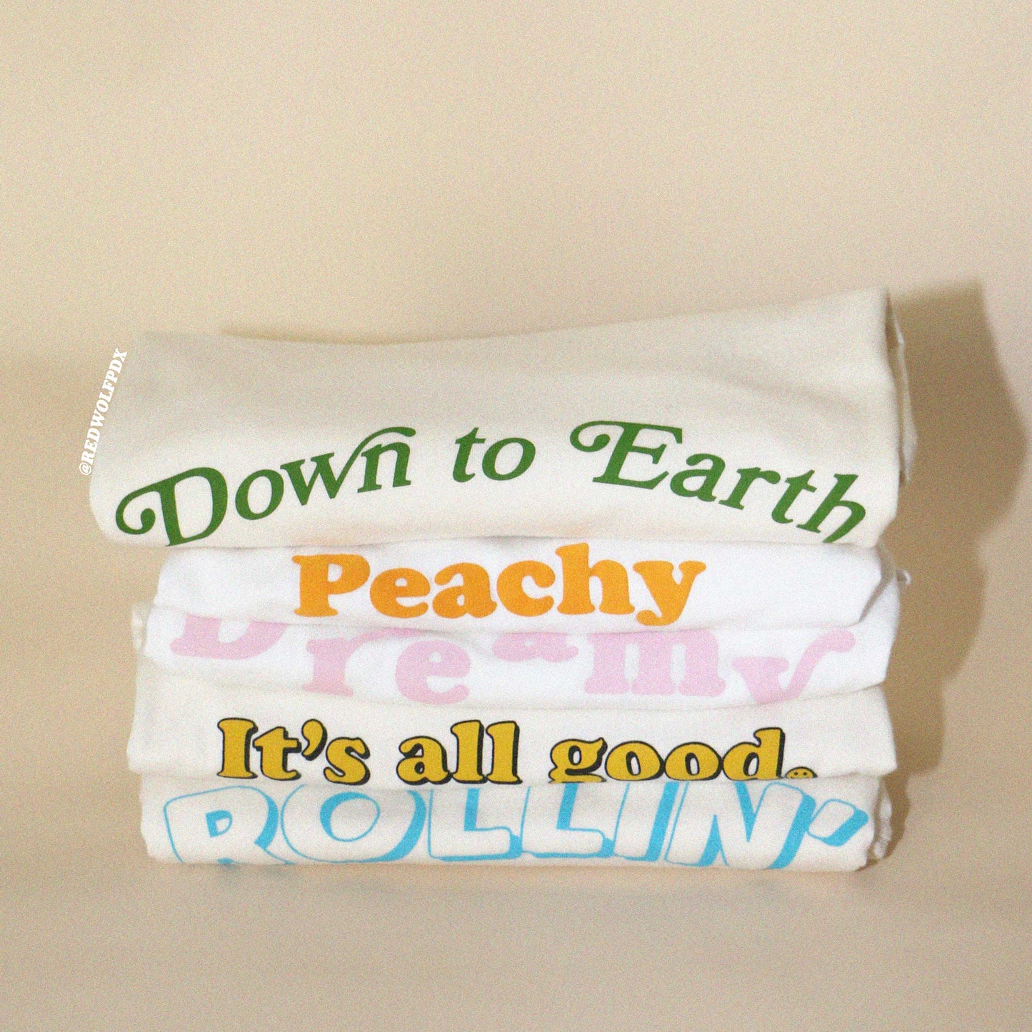 Stack of graphic tees with colorful text on a beige background