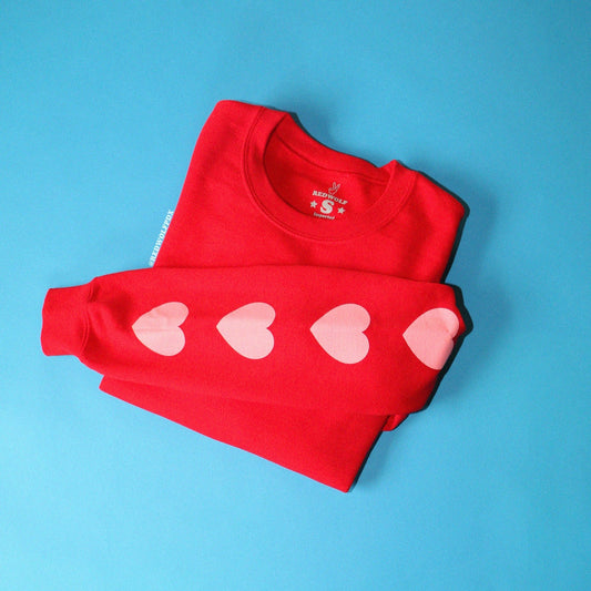 heart printed sleeves on red crewneck sweatshirt folded on blue backdrop