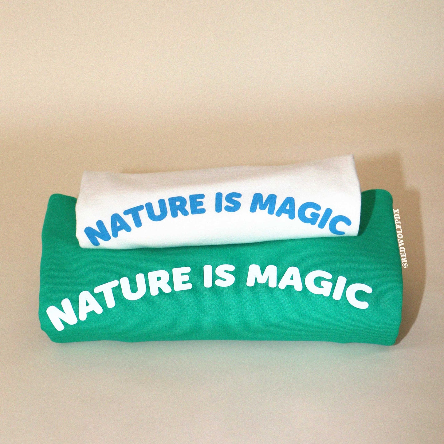 'nature is magic' graphic tee and sweatshirt folded on backdrop