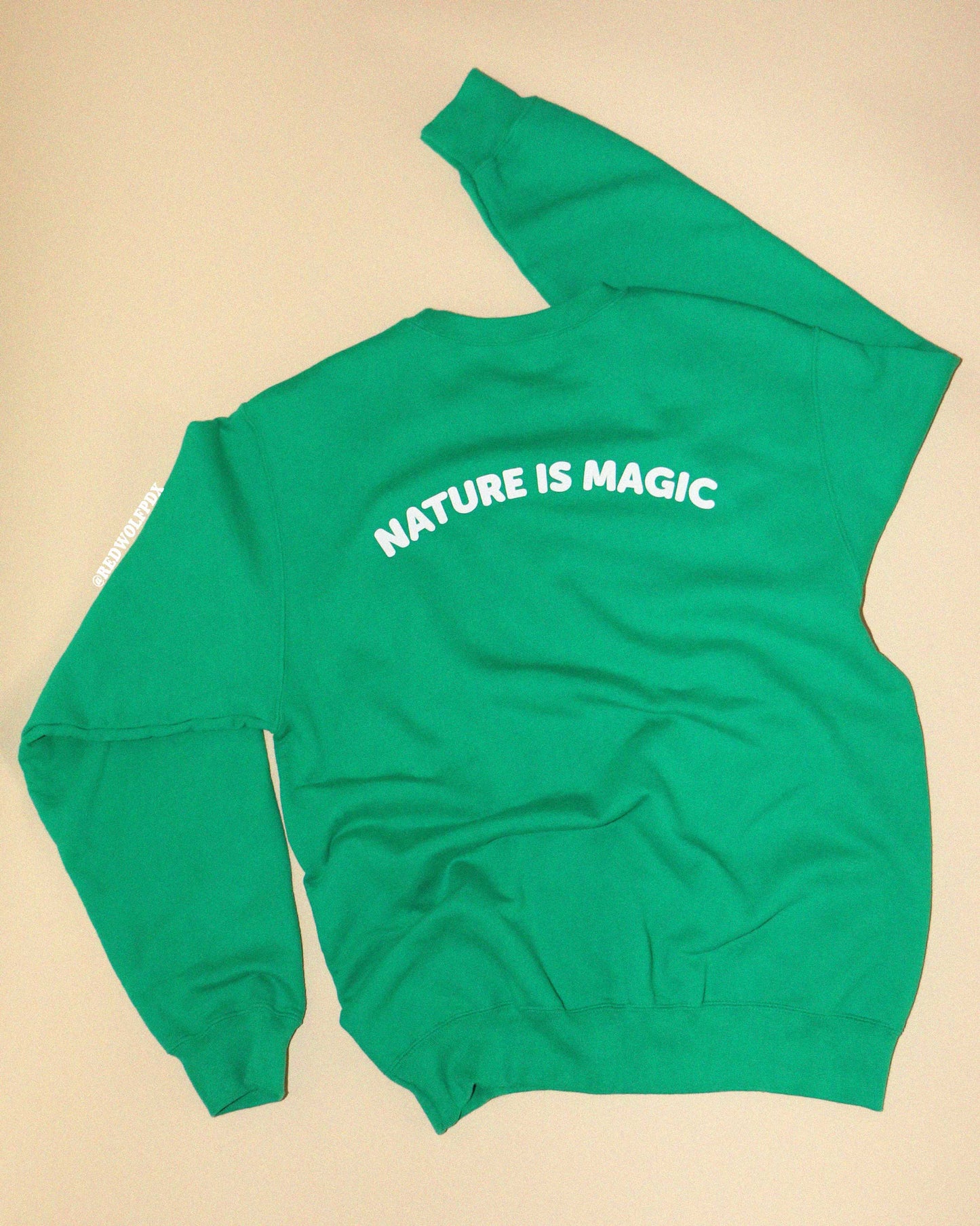 Green sweatshirt with 'NATURE IS MAGIC' text against  backdrop