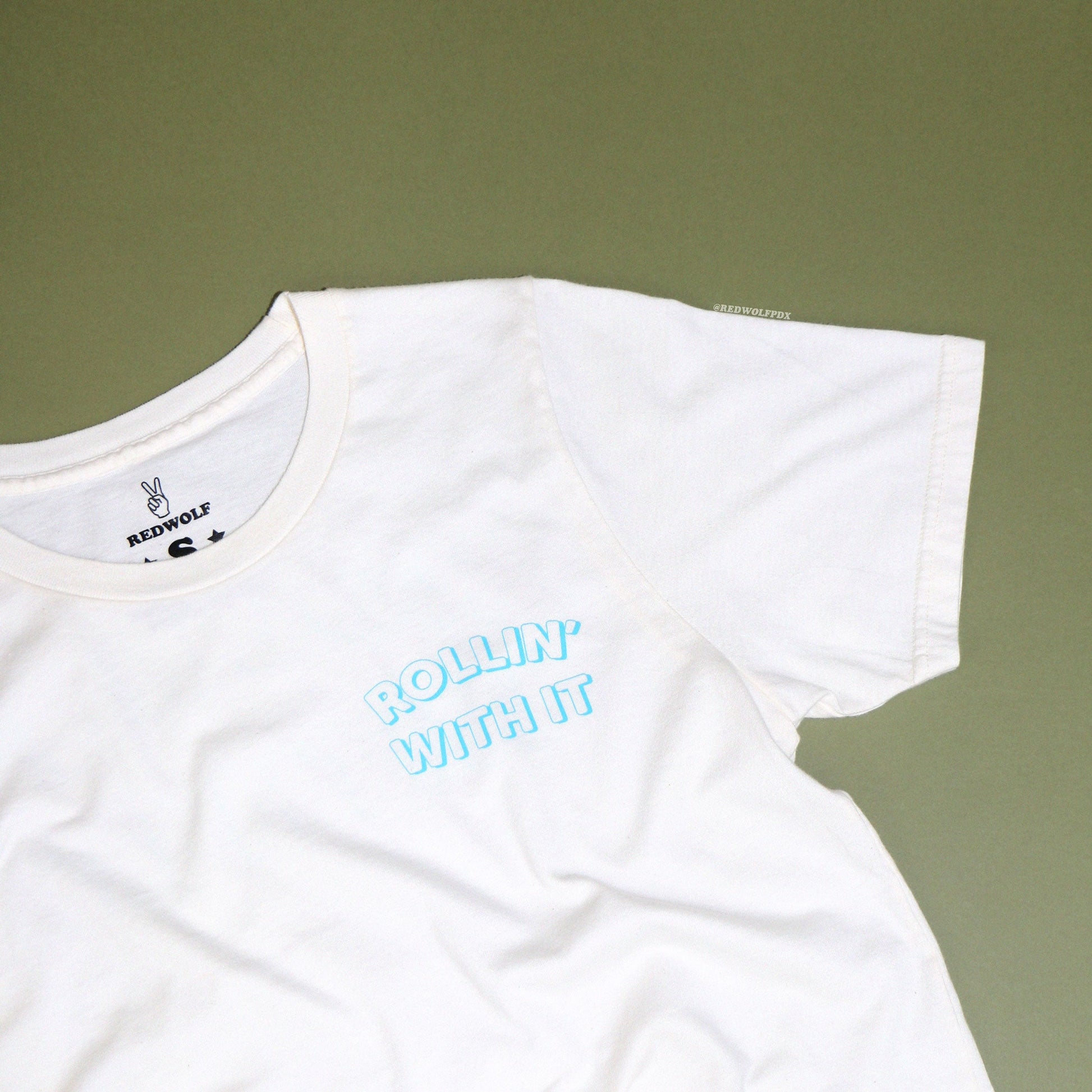 Beige white graphic tee with text 'ROLLIN' WITH IT' on a vintage green background