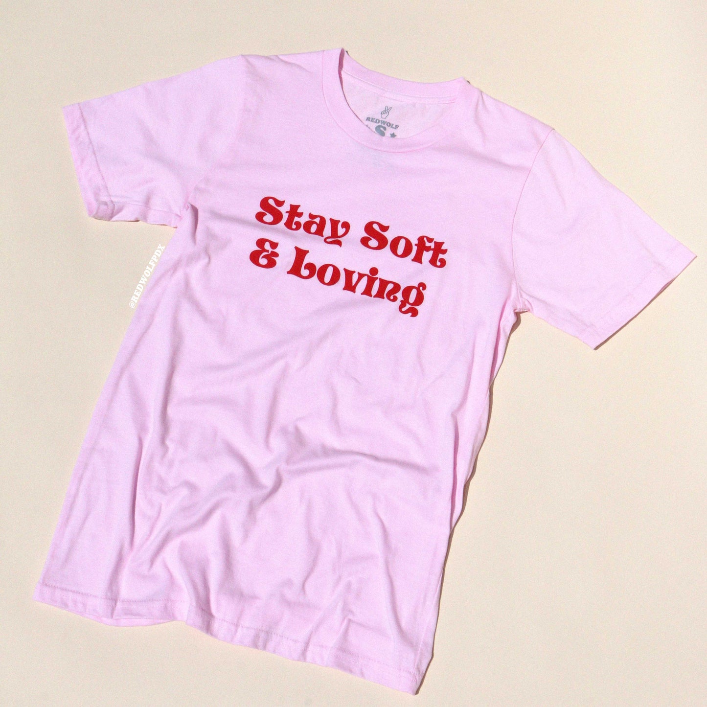 Pink t-shirt with 'Stay Soft & Loving' text on a beige background