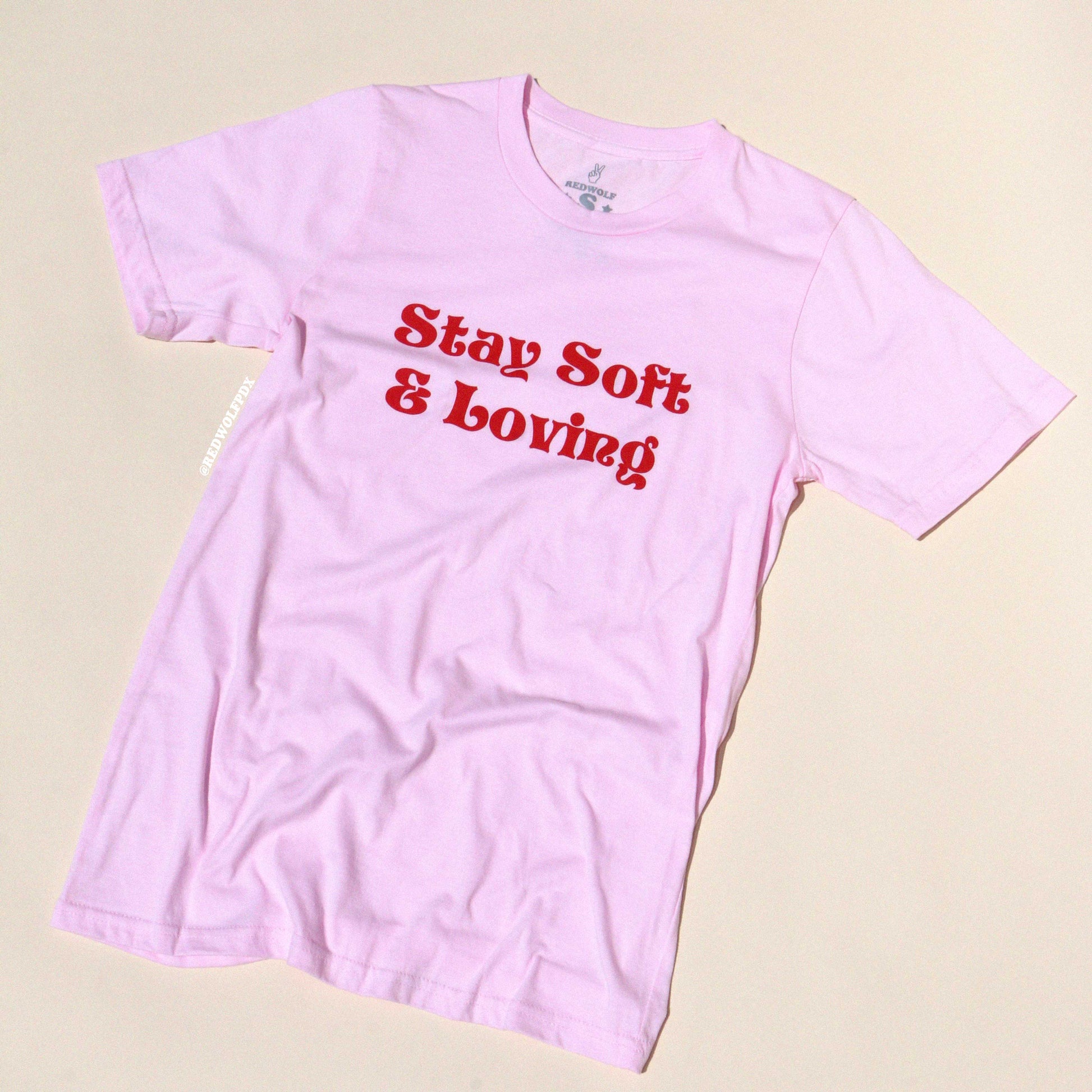 Pink t-shirt with 'Stay Soft & Loving' text on a beige background