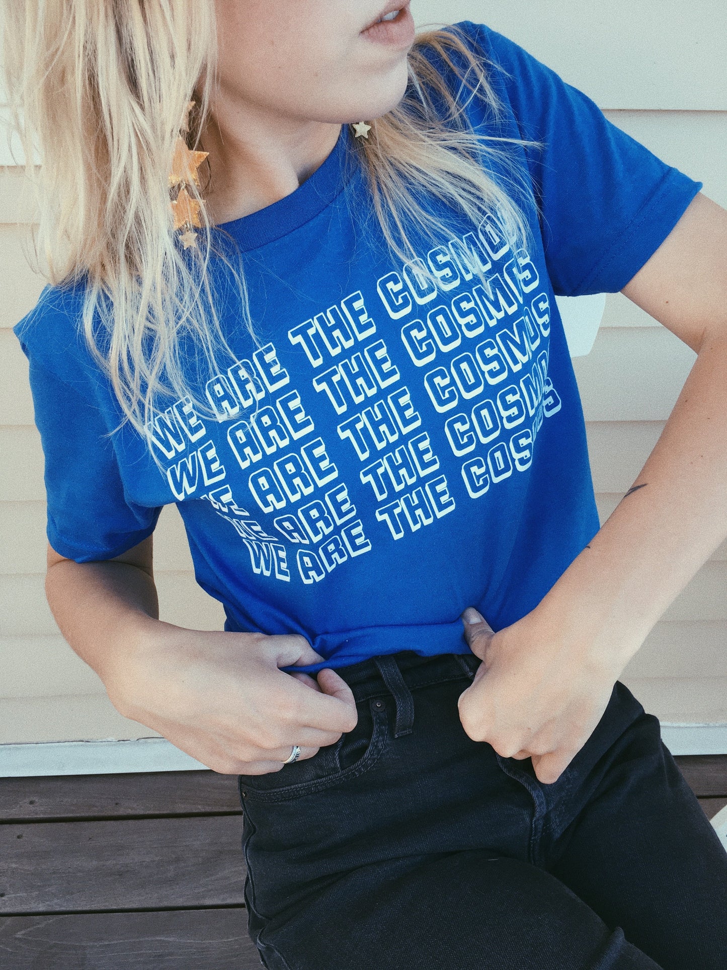 bright blue graphic tee with text 'WE ARE THE COSMOS' screen printed in white ink down the front being worn