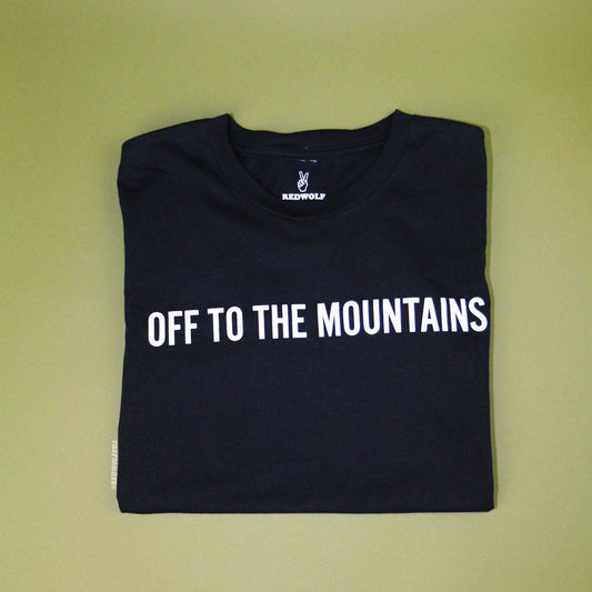 off to the mountains graphic tee folded on green backdrop