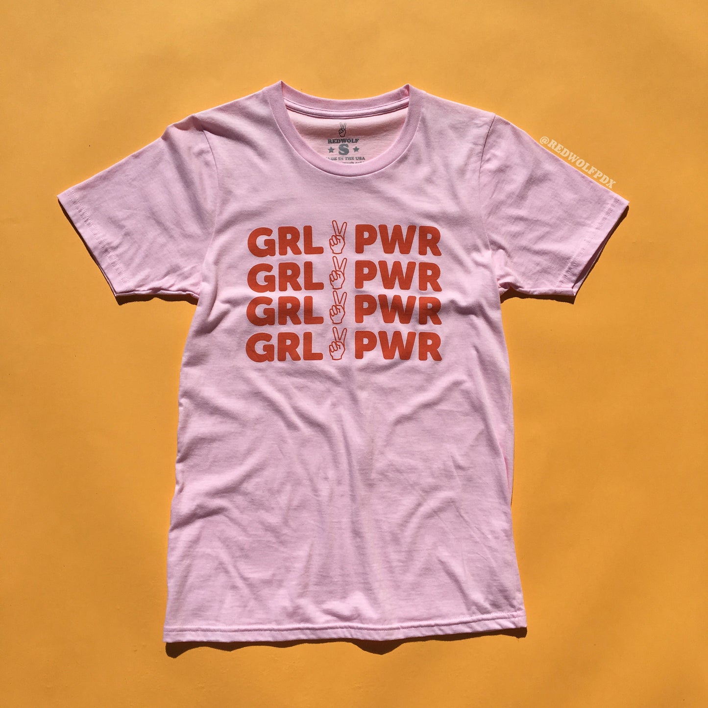 pink tee with text 'GRL PWR' with peace sign graphic screen printed down the front against a yellow background