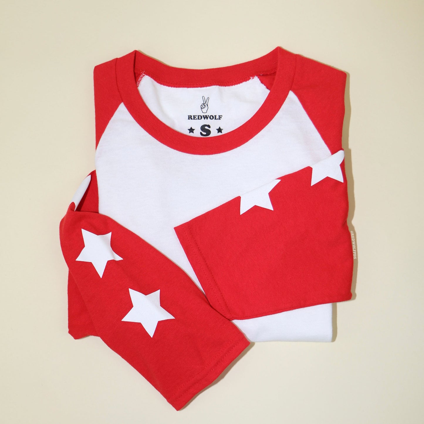folded vintage inspired raglan with white stars screen printed down the red sleeves  against a beige background