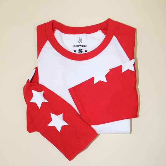folded vintage inspired raglan with white stars screen printed down the red sleeves  against a beige background
