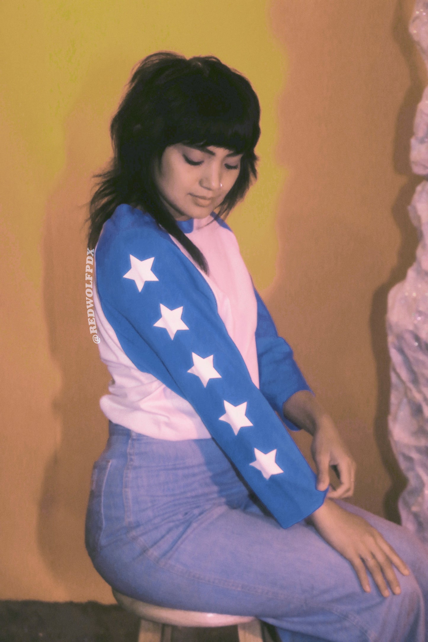 White and blue baseball shirt with white stars screen printed down the sleeves being worn on a space backdrop