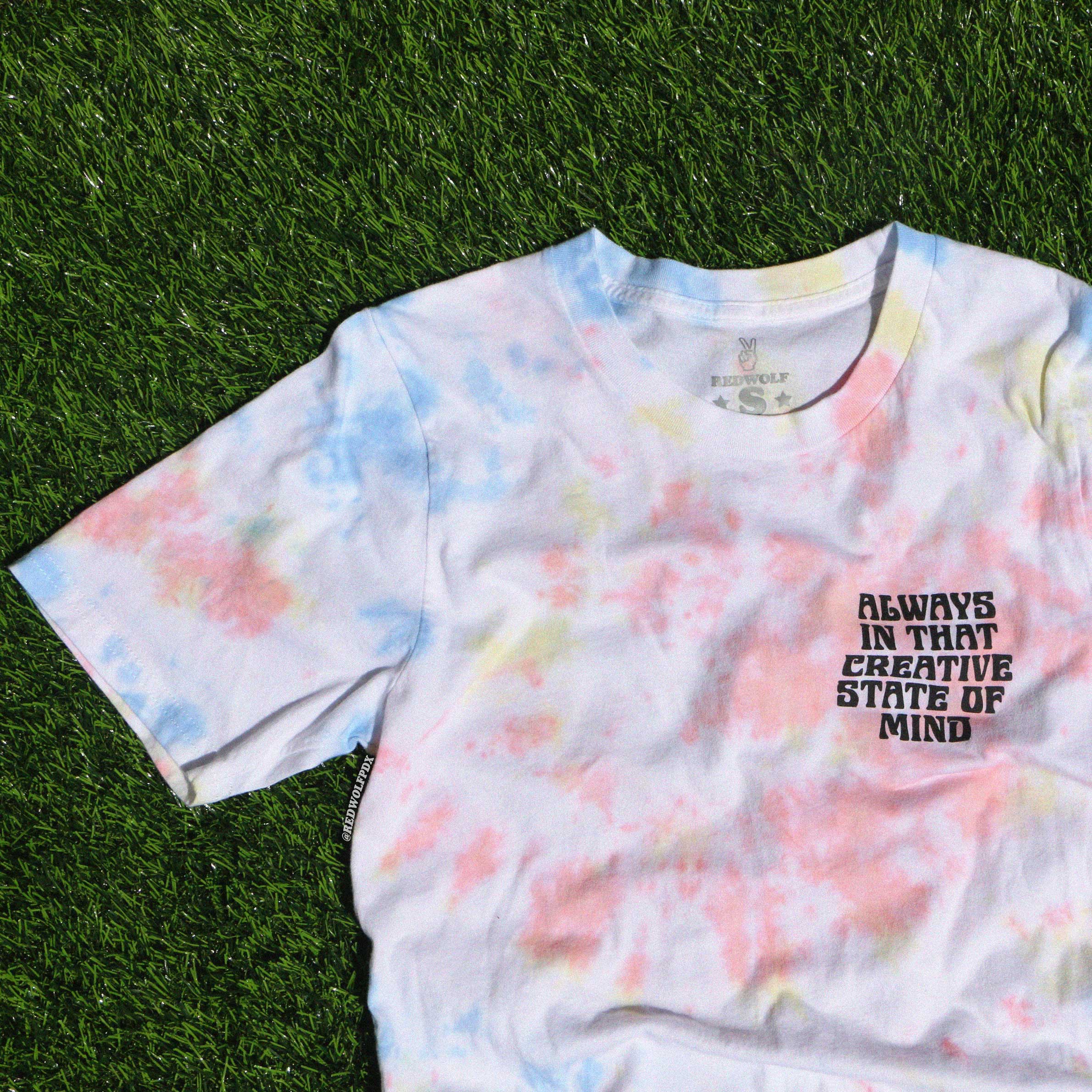 A tie-dye t-shirt with a text design that reads 'ALWAYS IN THAT CREATIVE STATE OF MIND' on the chest.