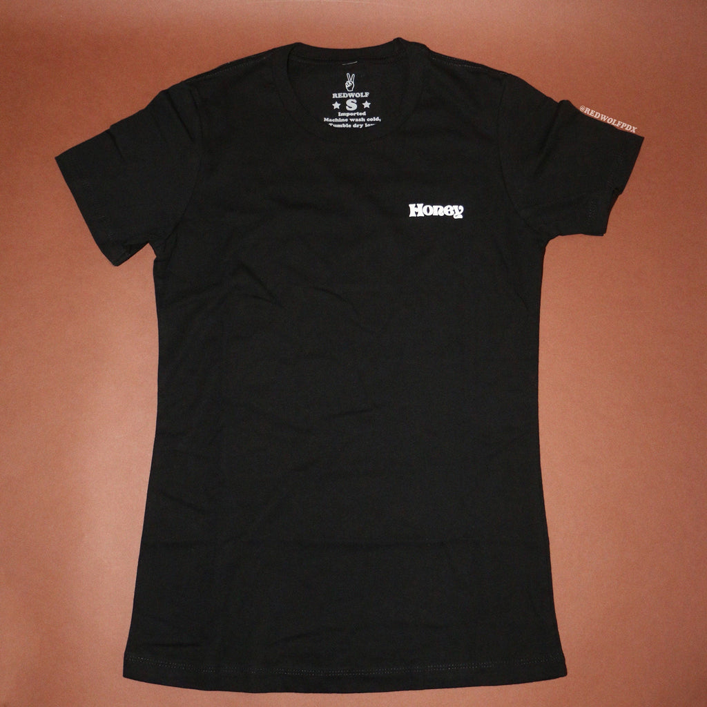 Black fitted tee with text 'Honey' on corner of chest against brown backdrop