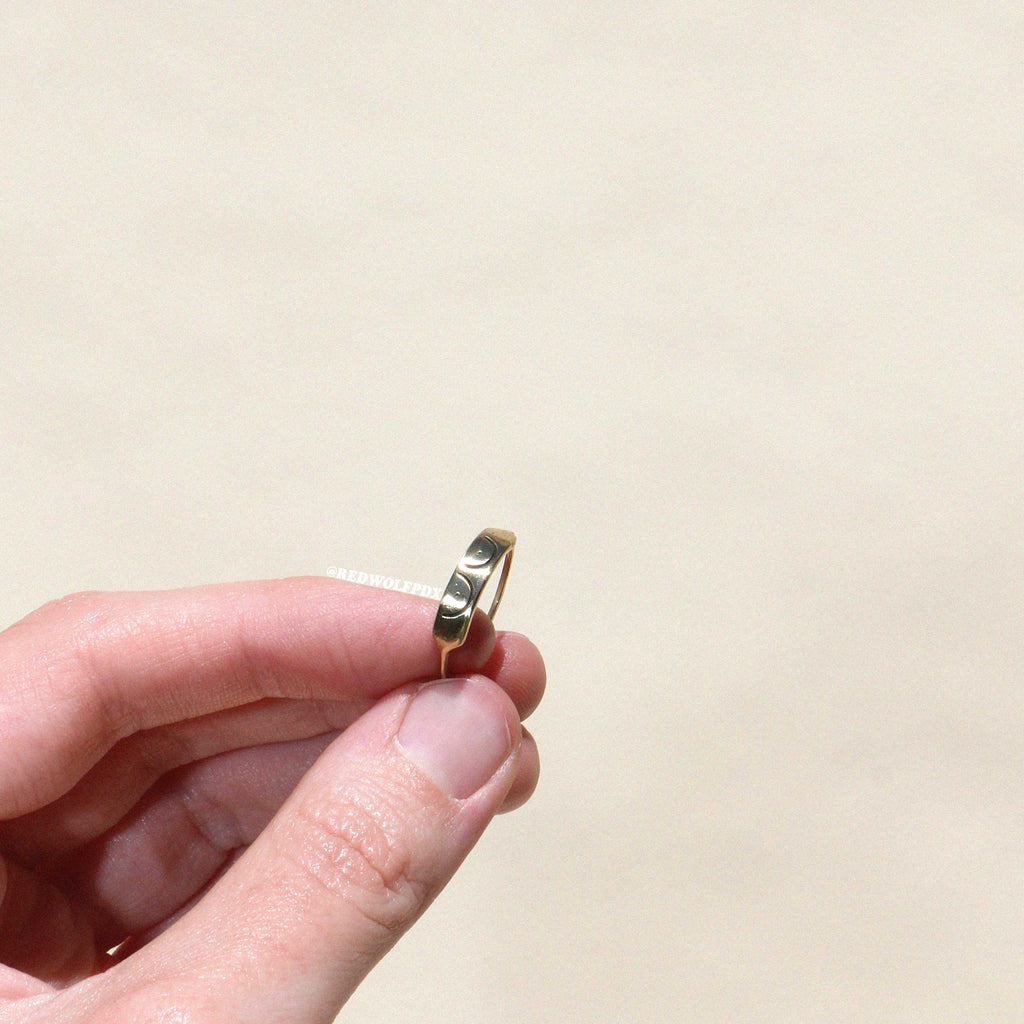 brass ring with boob illustration etched across it being held against a beige backdrop