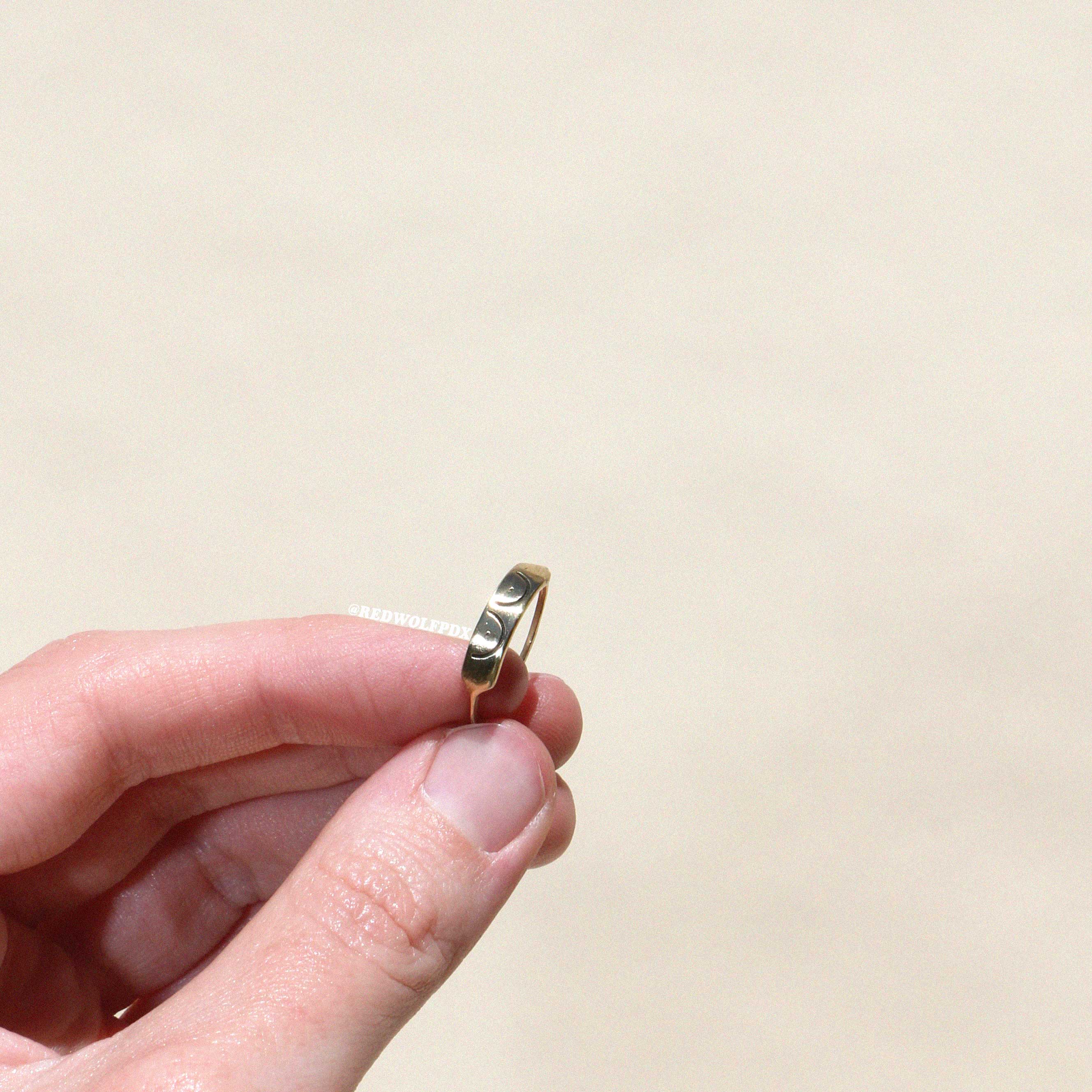 brass ring with boob illustration etched across it being held against a beige backdrop