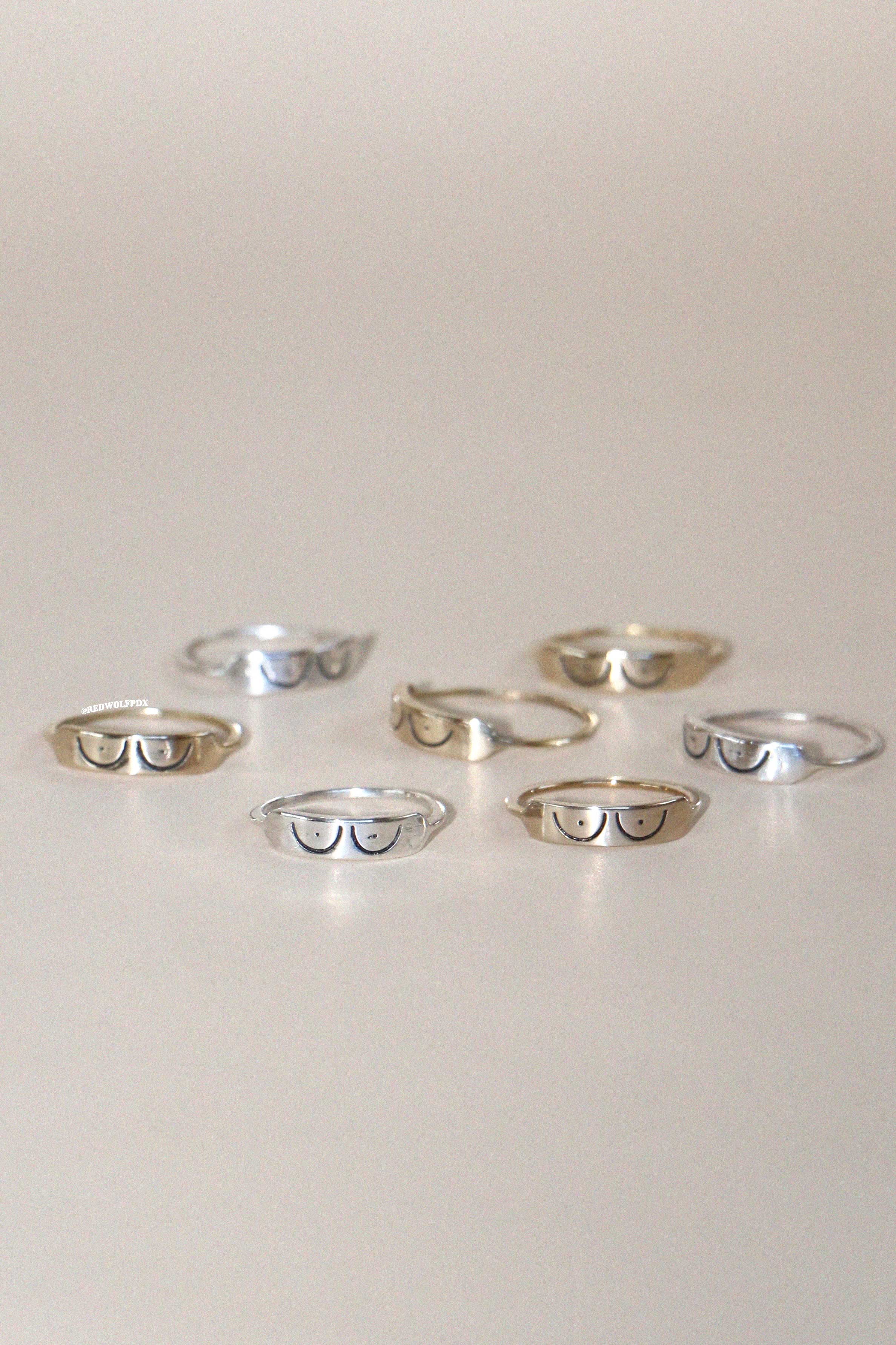 A collection of rings with a boob illustration etched into them, displayed on a light background.
