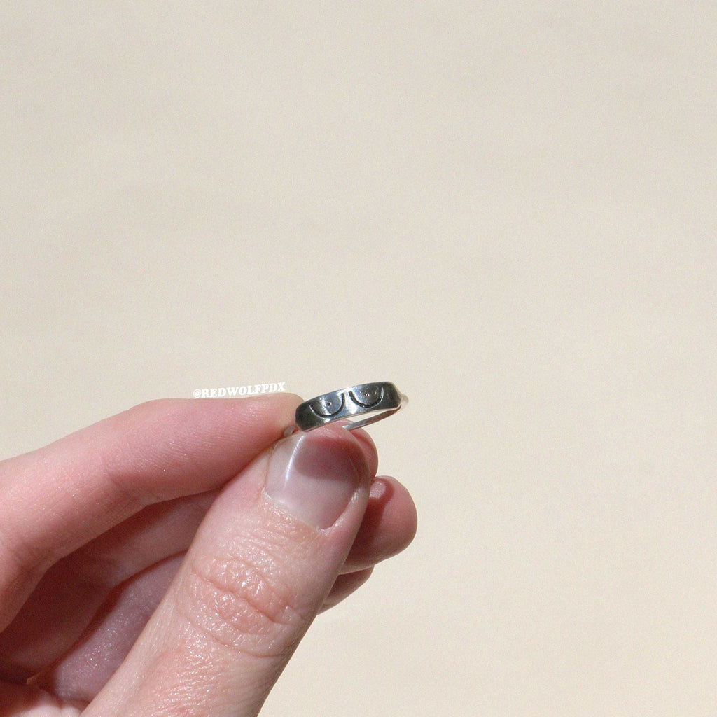 sterling silver ring with boob illustration etched across it being held against a beige backdrop
