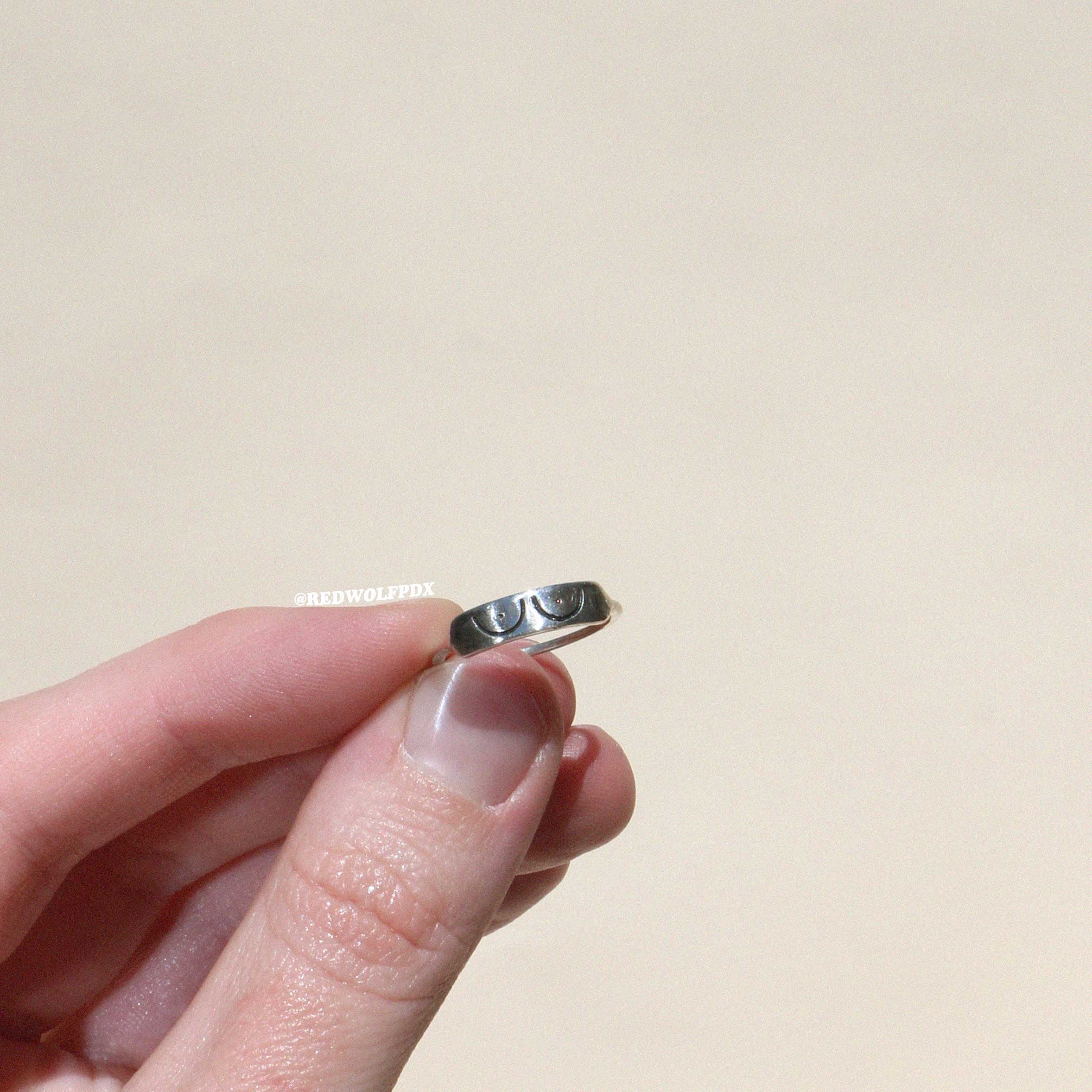 sterling silver ring with boob illustration etched across it being held against a beige backdrop