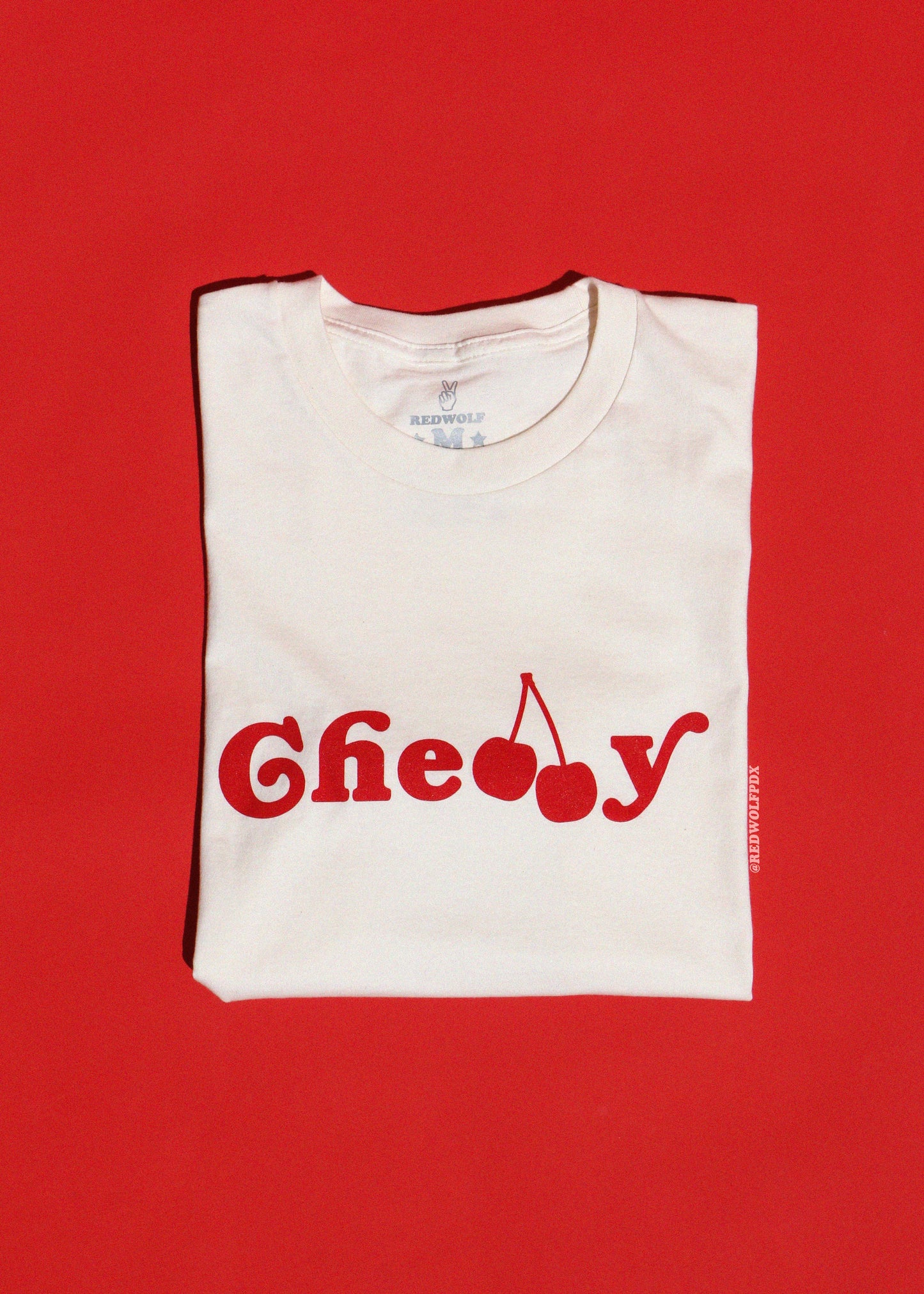 Folded white t-shirt with red text and cherry graphic on a red background