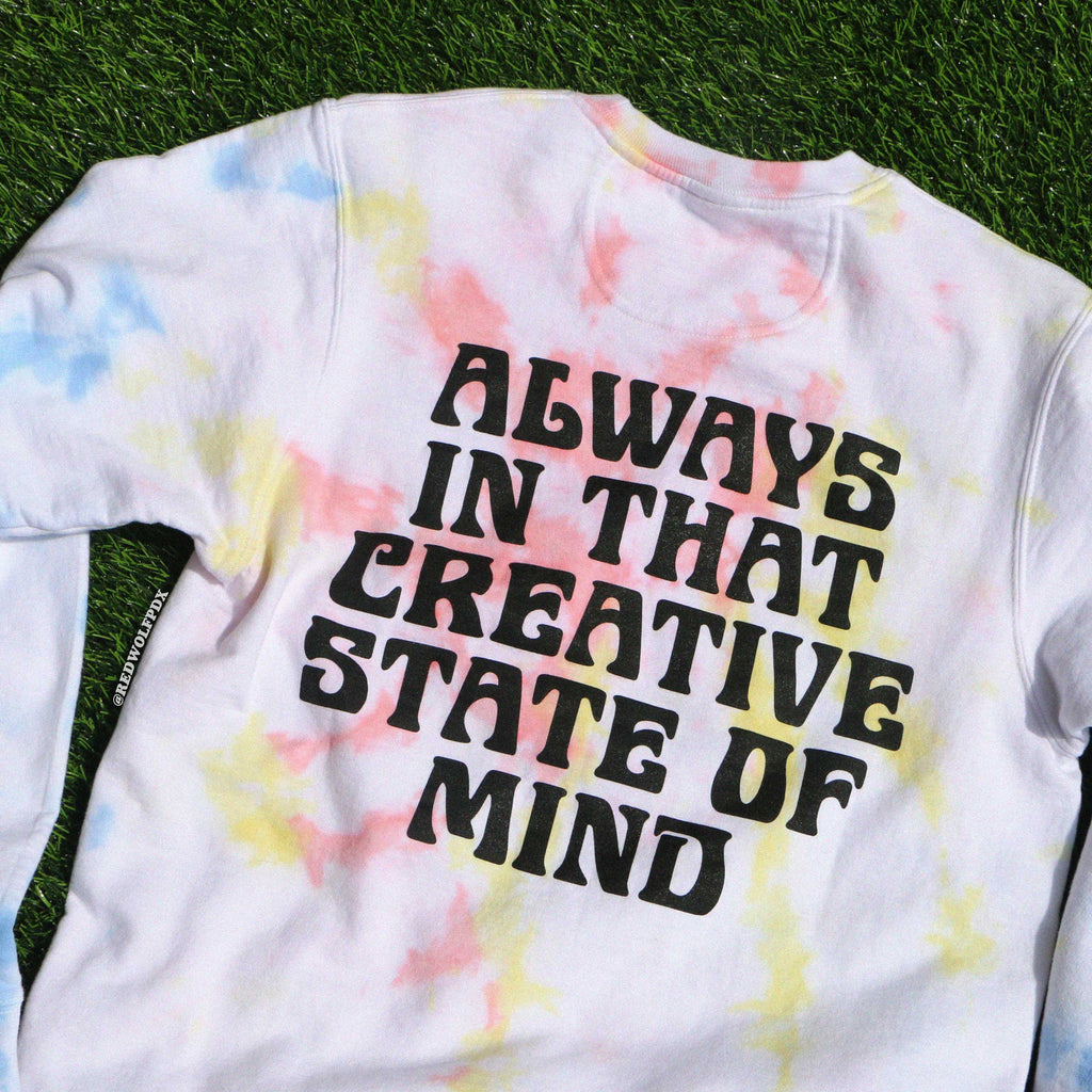 Tie-dye crewneck sweatshirt with text  'ALWAYS IN THAT CREATIVE STATE OF MIND' on a grass background