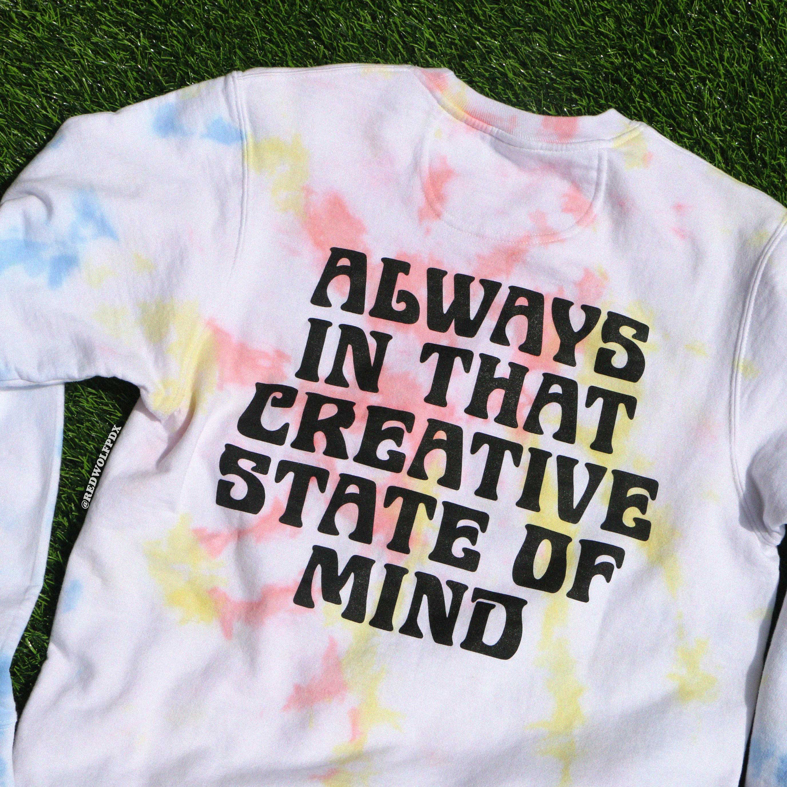 Tie-dye crewneck sweatshirt with text  'ALWAYS IN THAT CREATIVE STATE OF MIND' on a grass background
