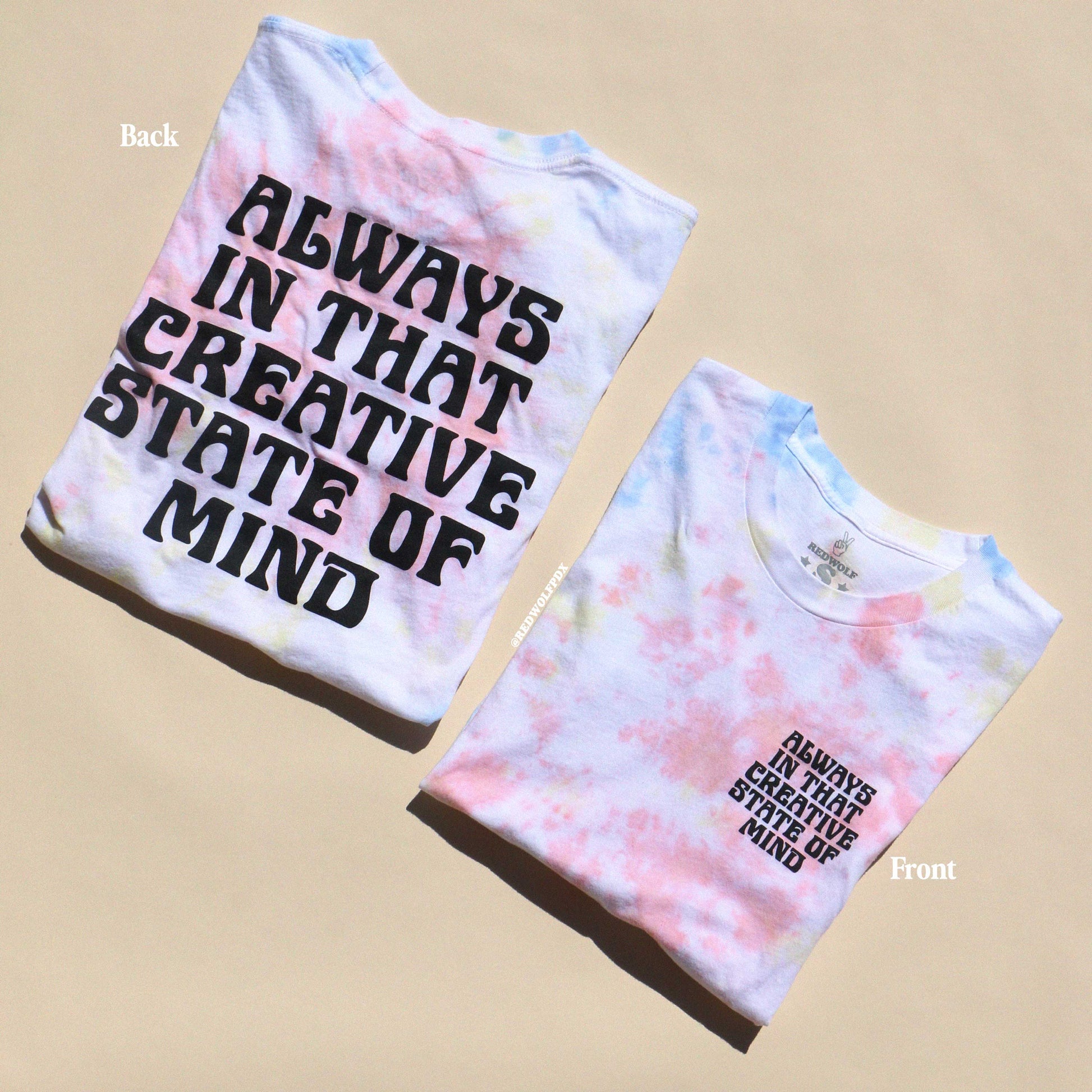 Two tie-dye t-shirts with text 'ALWAYS IN THAT CREATIVE STATE OF MIND' printed on them, one displayed front side up and the other back side up showing the text on the reverse.