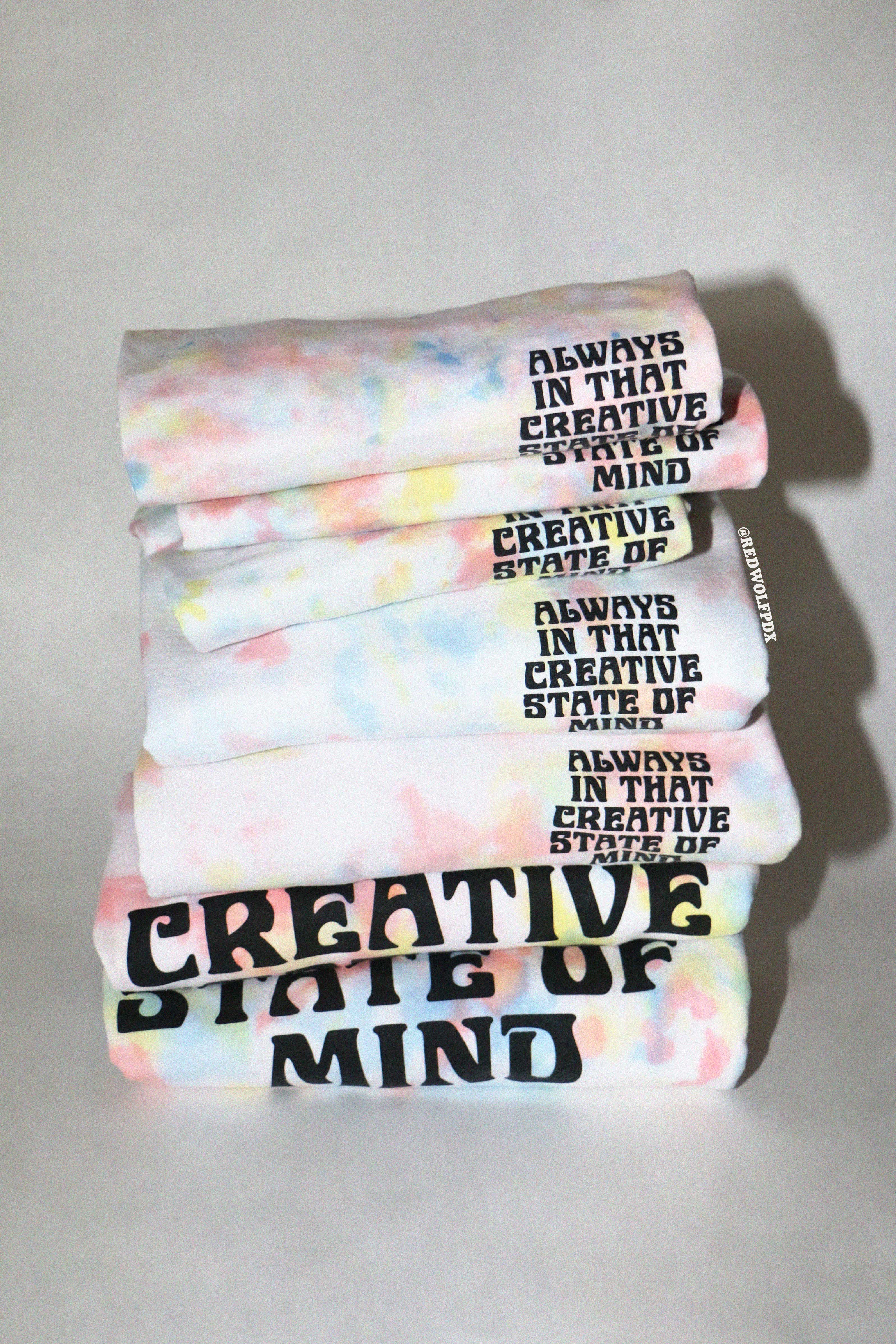 Stack of tie dye tees and crewnecks with the text 'Always in that creative state of mind' text on a white background