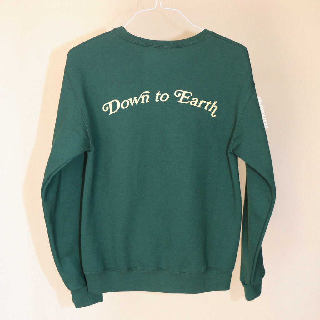 Forest green crewneck sweatshirt with 'Down to Earth' text on a beige background