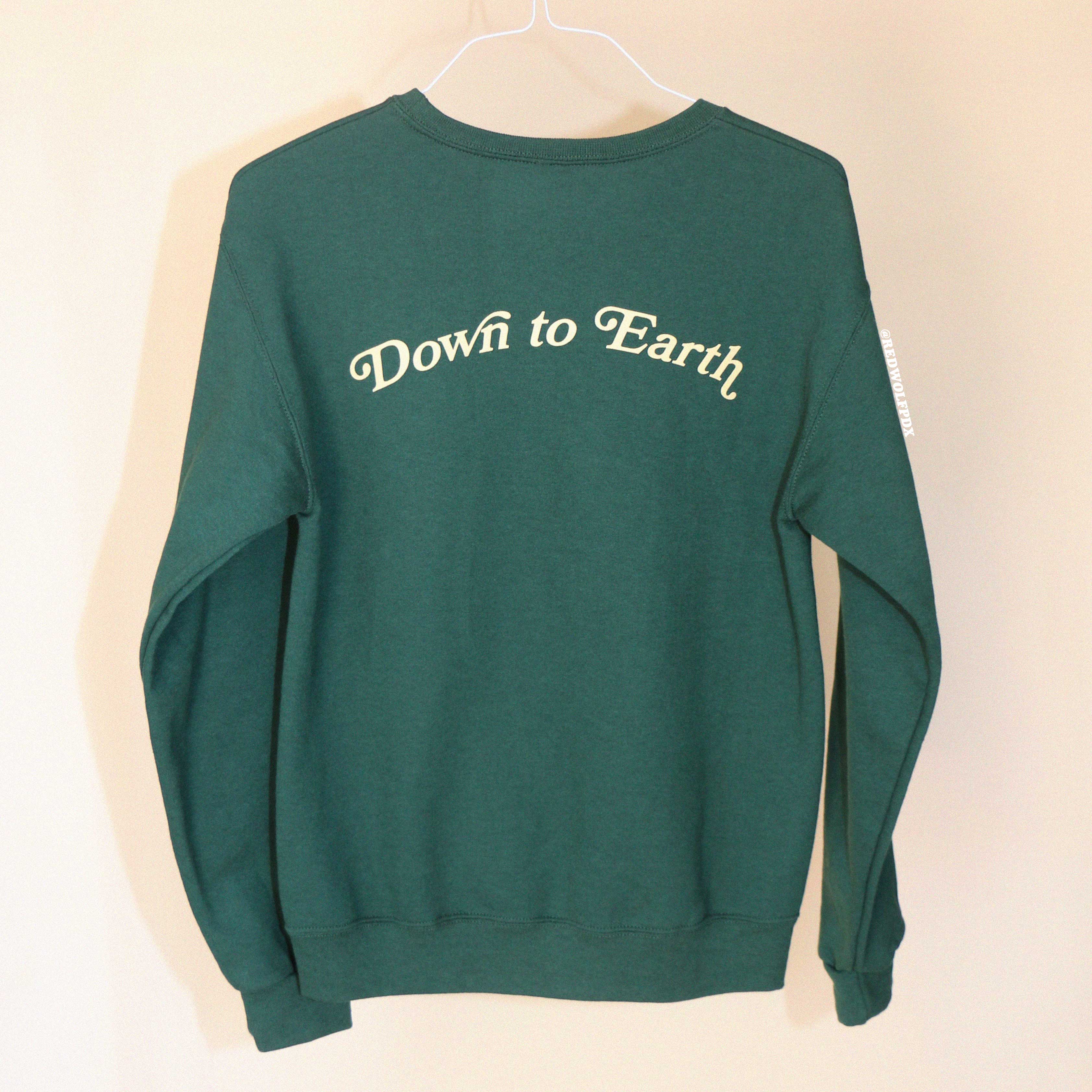 Forest green crewneck sweatshirt with 'Down to Earth' text on a beige background