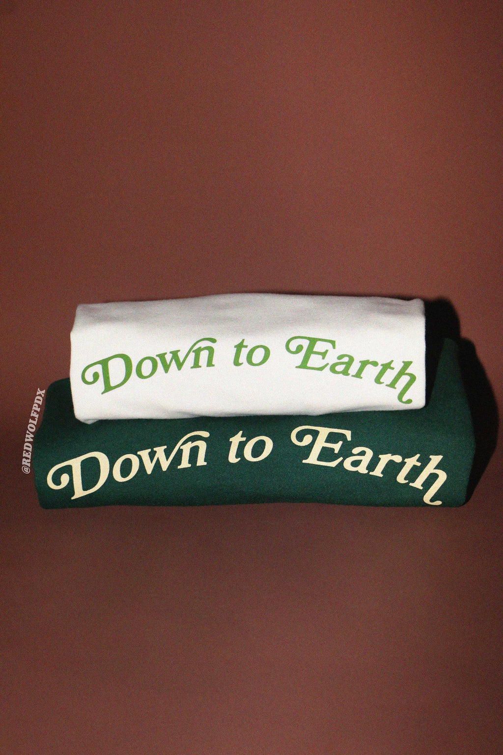 white tee and forest green crewneck sweatshirt stacked on a brown background with 'Down to Earth' text.