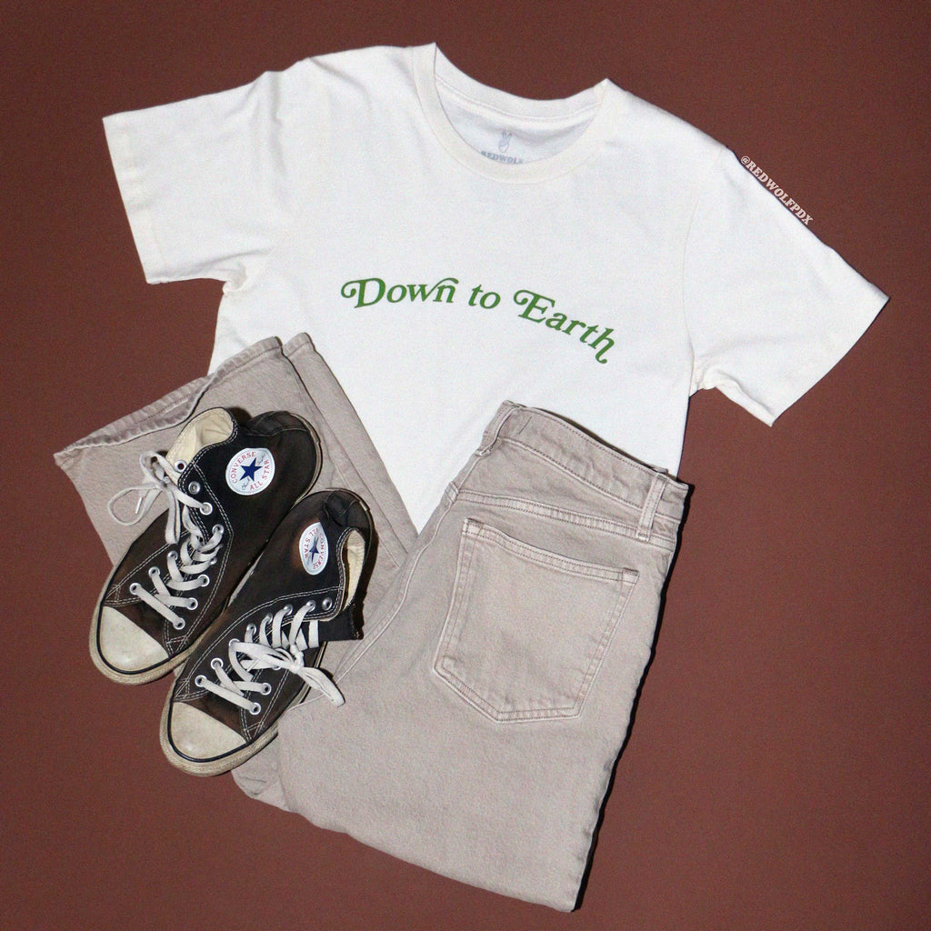 Graphic tee with text 'Down to Earth' with khaki jeans and sneakers for flatlay against brown backdrop