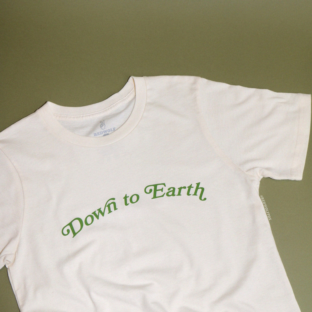 Beige graphic tee with text 'Down to Earth' in green ink against green backdrop