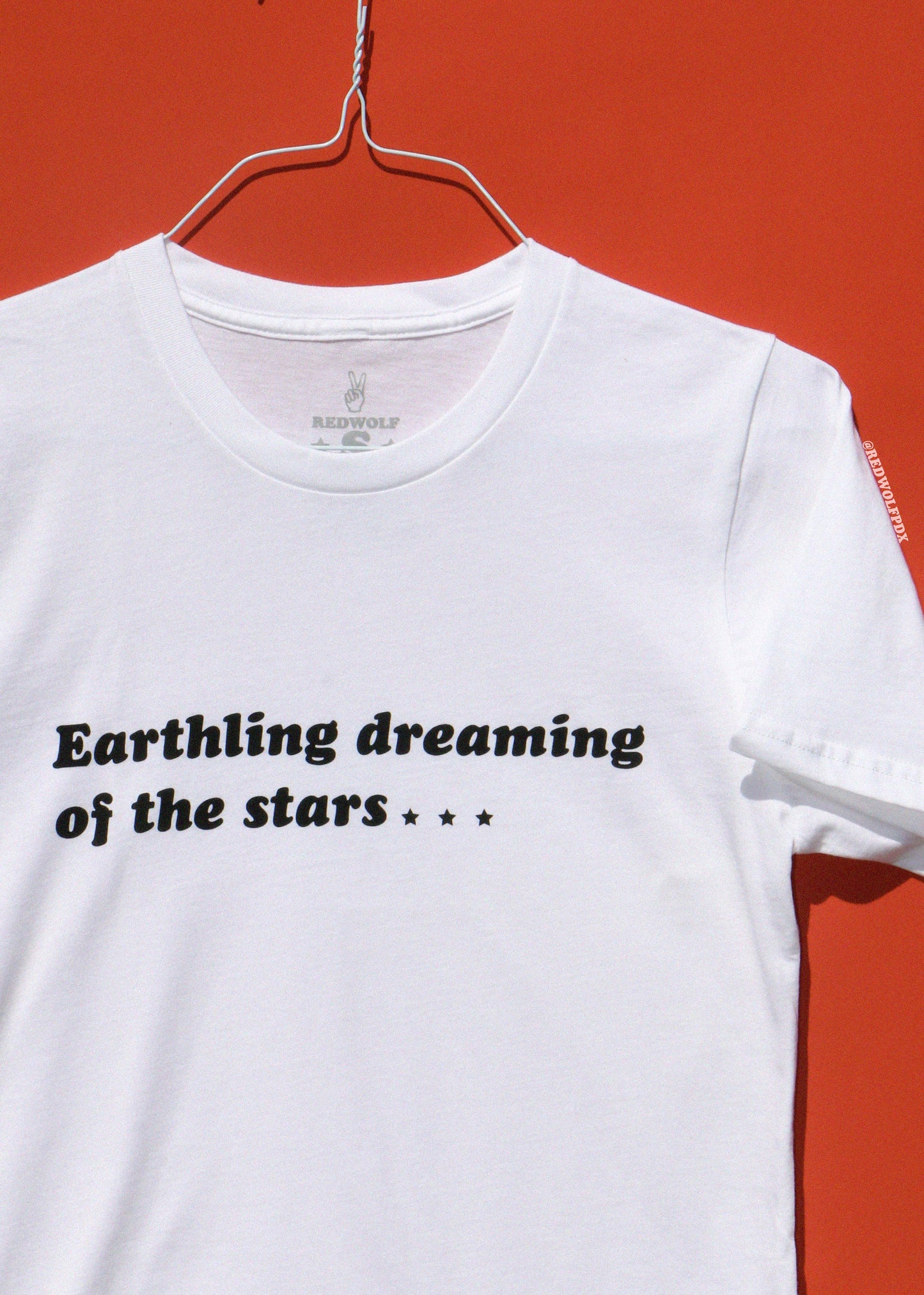 White t-shirt with text 'Earthling dreaming of the stars' on a red background