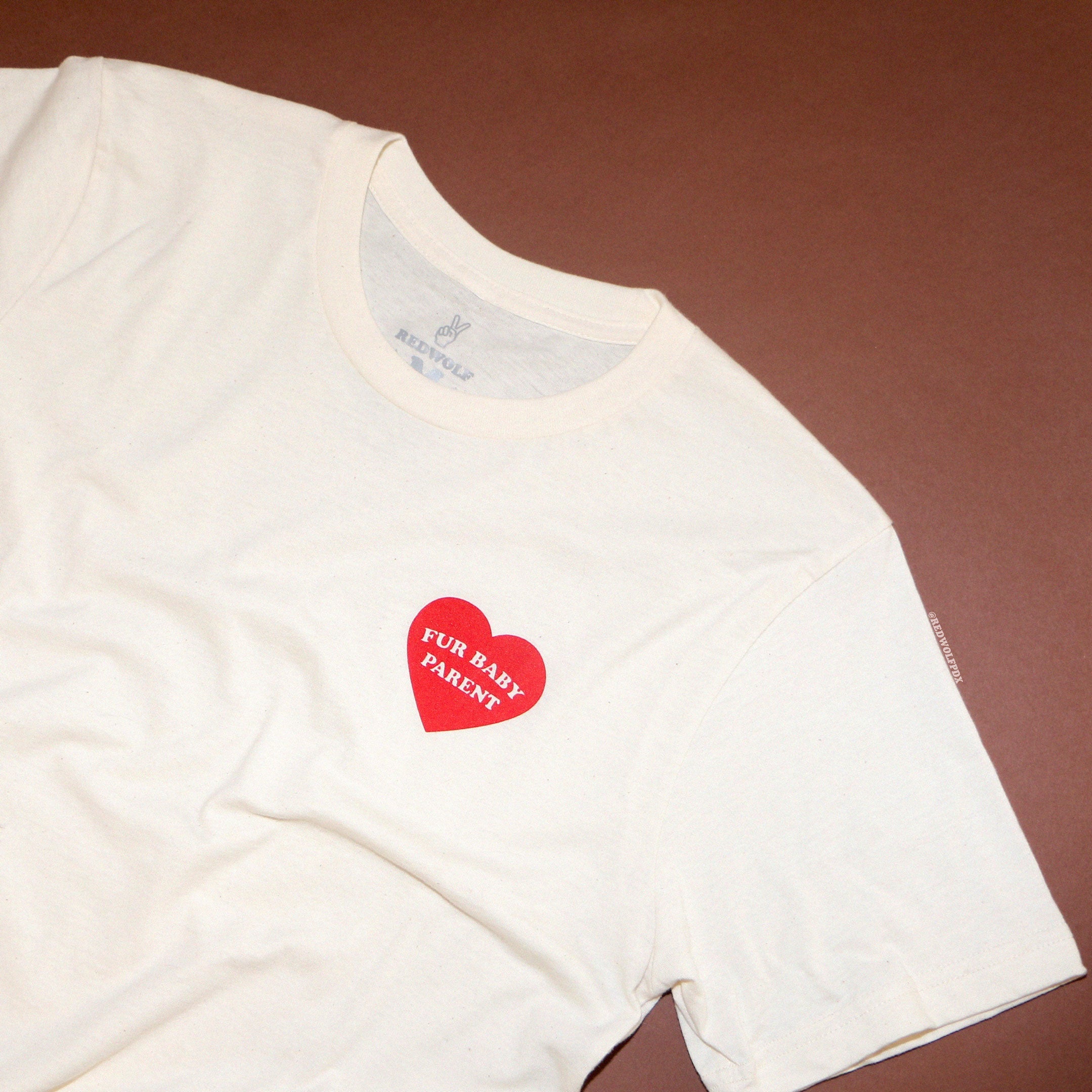 beige graphic tee with text 'FUR BABY PARENT' heart graphic in red ink screen printed on front against brown background