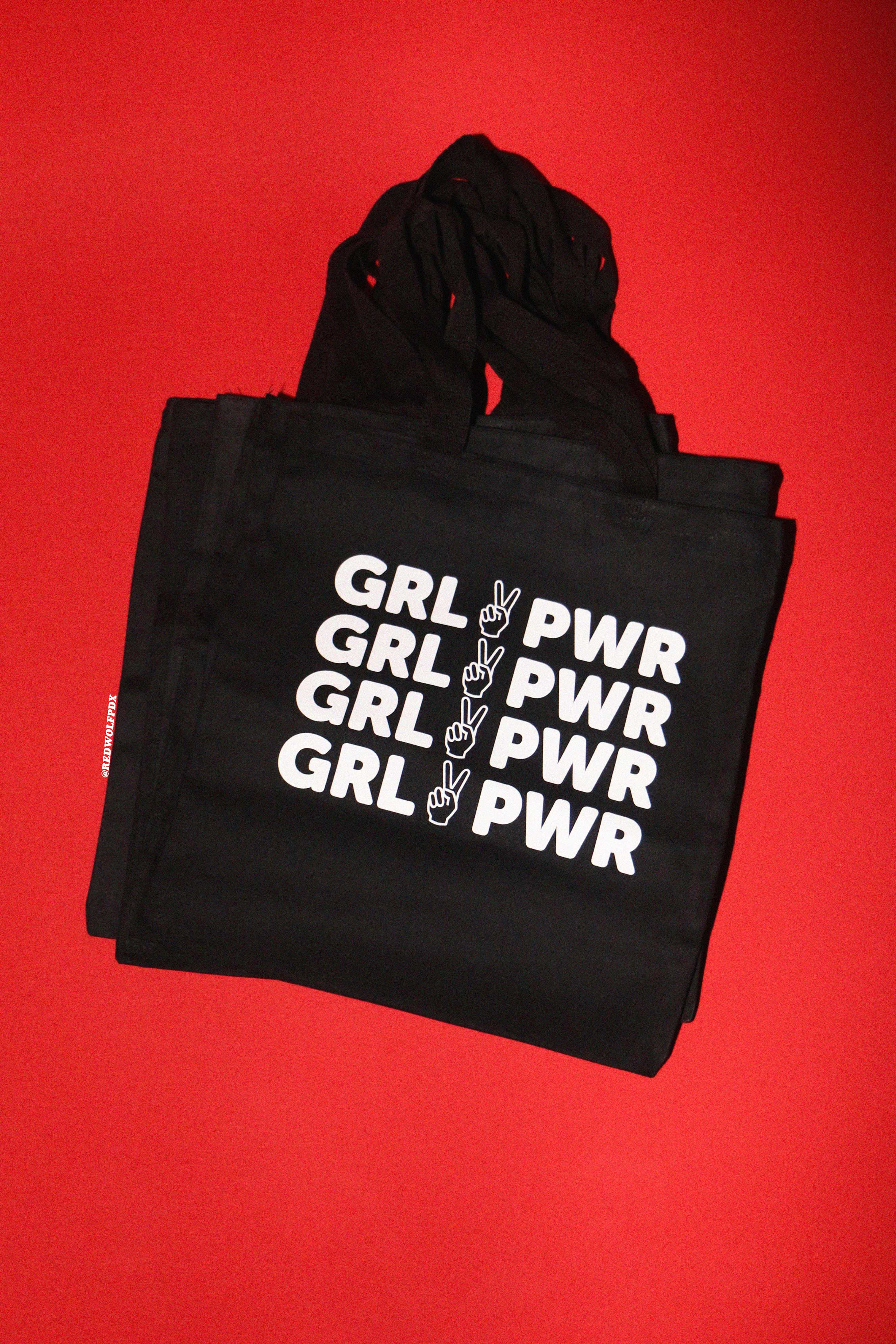 stack of black canvas tote bags with 'GRL PWR' text on a red background