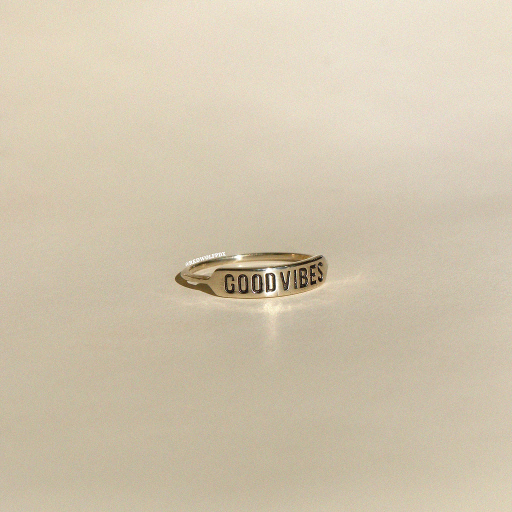 brass ring with text 'GOOD VIBES' engraved across it on beige  background