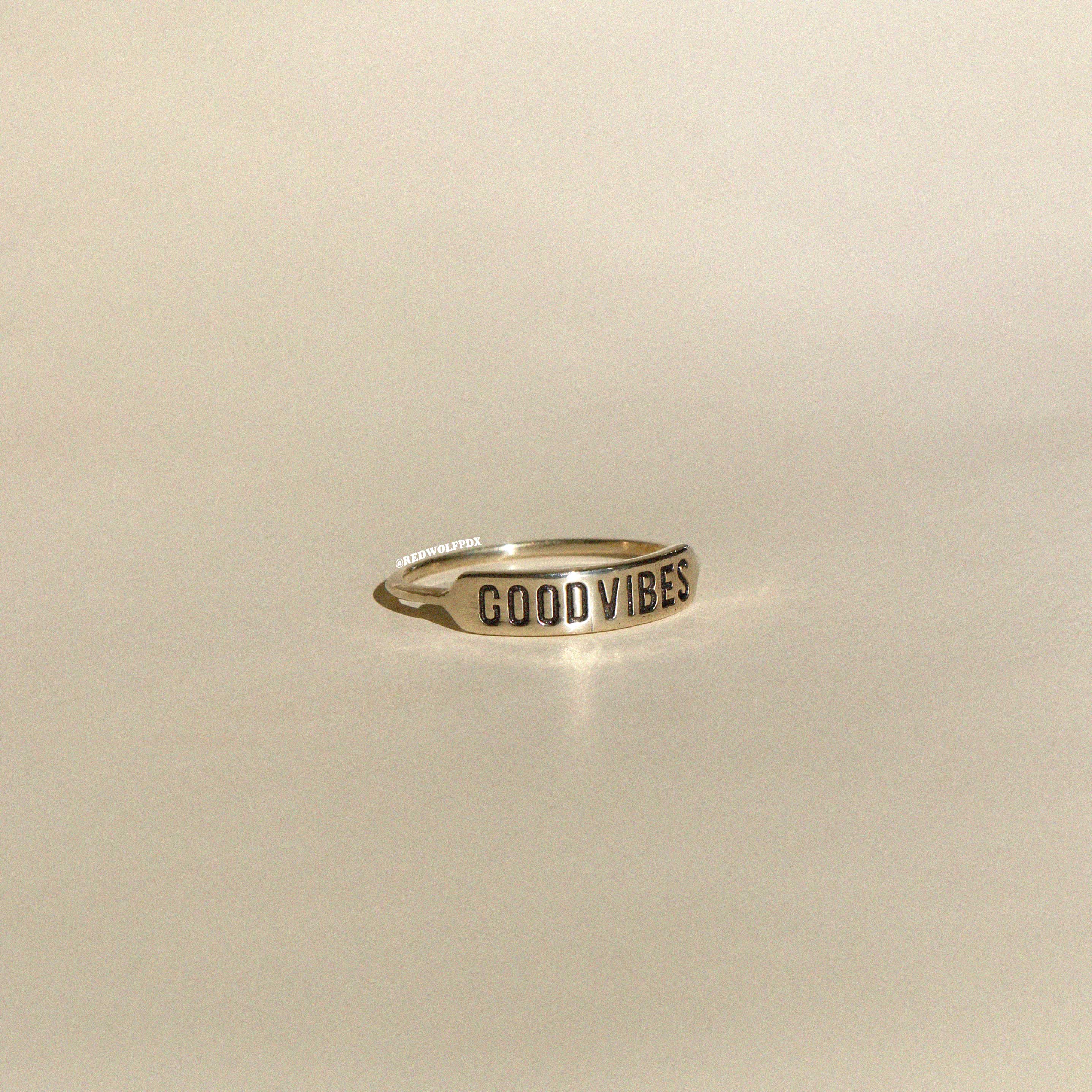 brass ring with text 'GOOD VIBES' engraved across it on beige  background