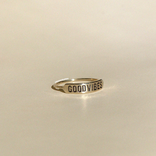 brass ring with text 'GOOD VIBES' engraved across it on beige  background