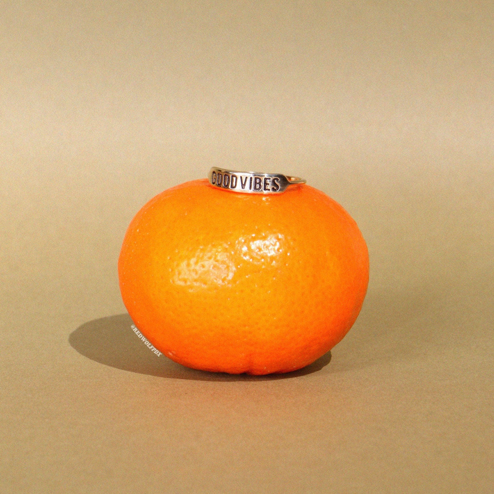 good vibes etched ring sitting on a tangerine on green backdrop
