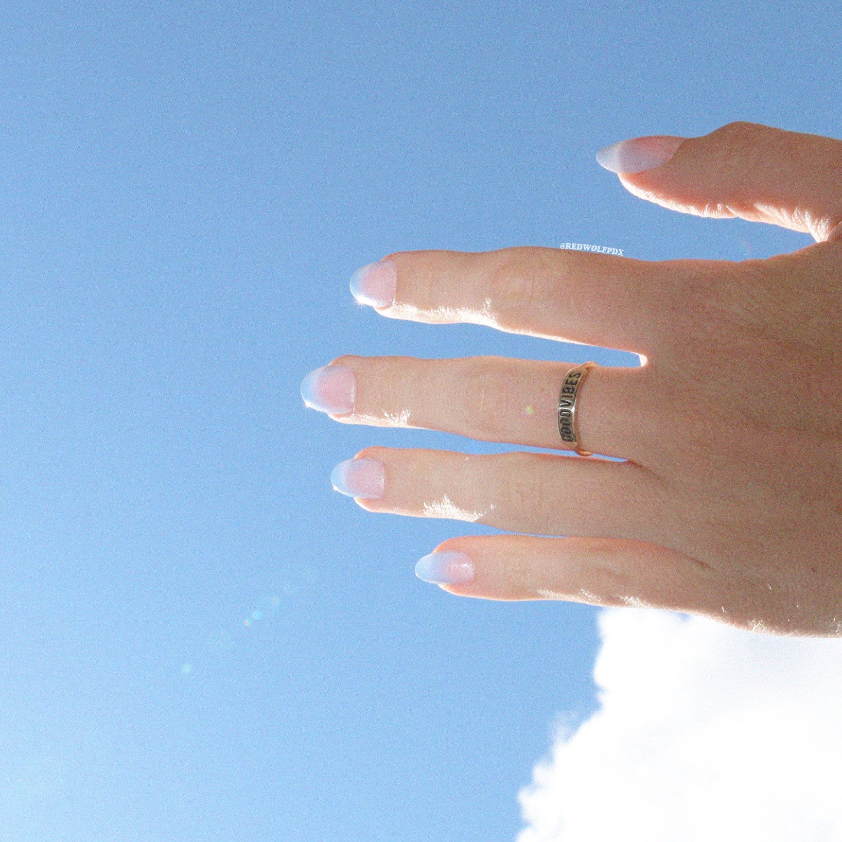 Brass ring with text 'GOOD VIBES' etched on band being worn with blue sky backdrop