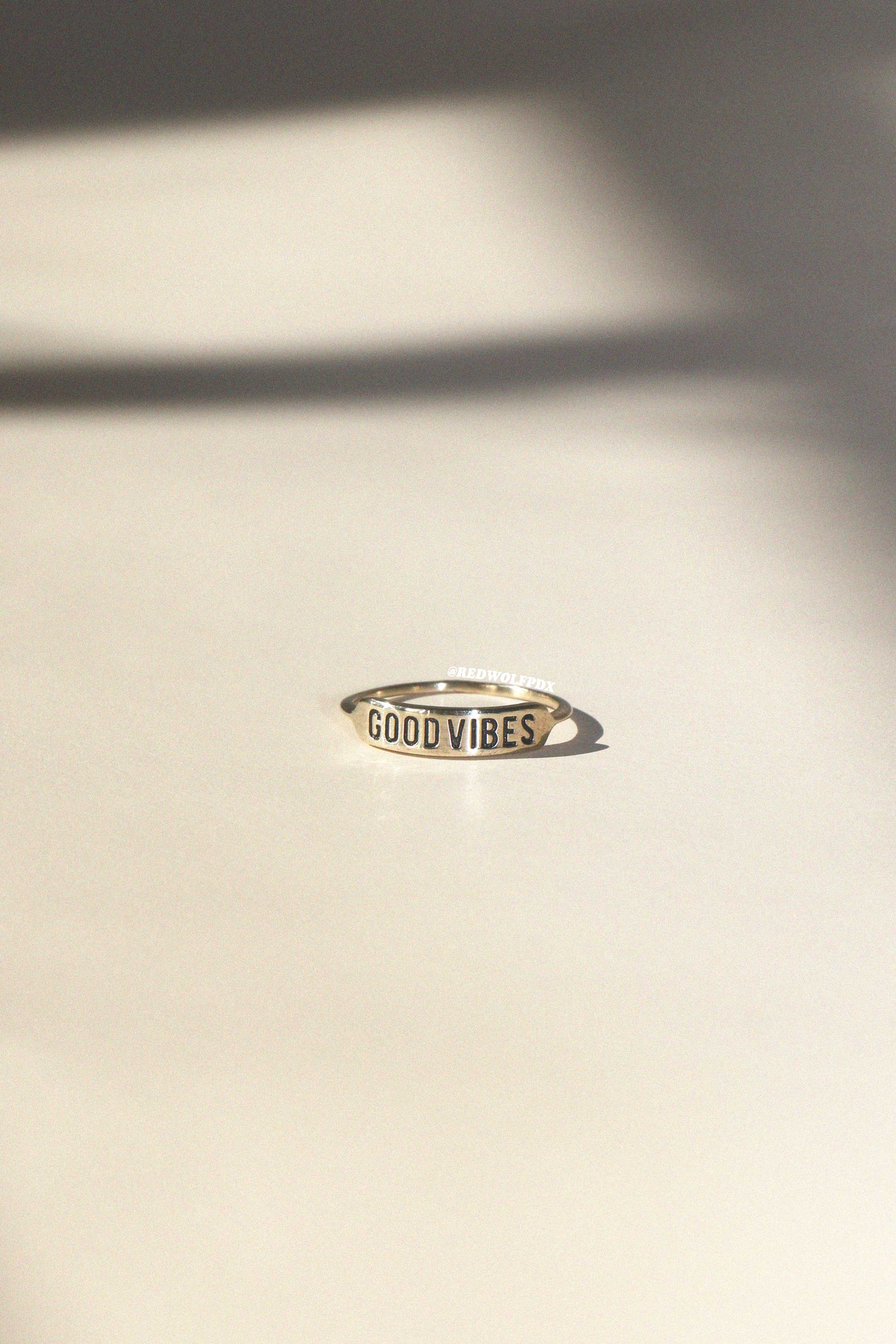 Gold ring with 'GOOD VIBES' engraving on a beige surface