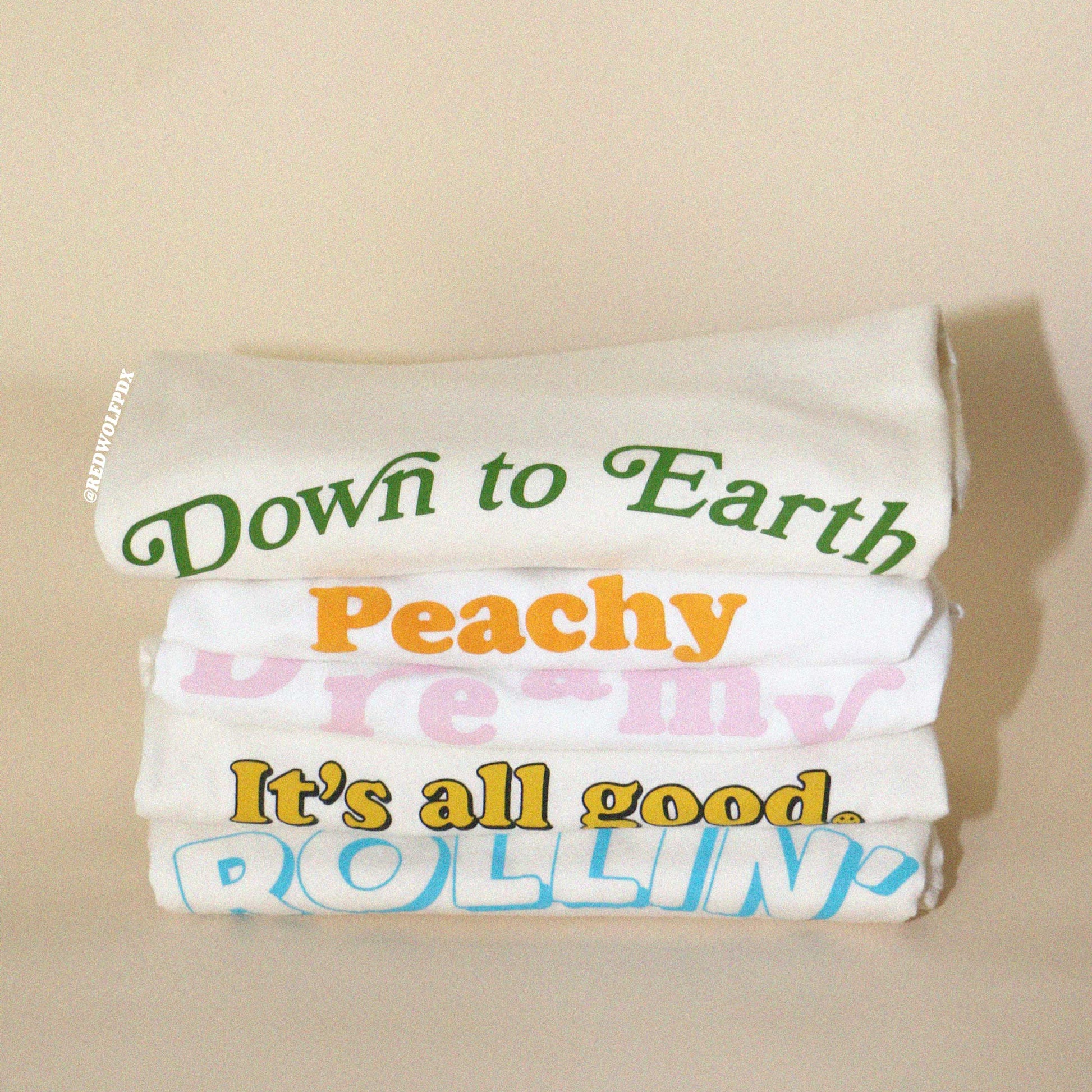 Stack of graphic tees with colorful text on a beige background