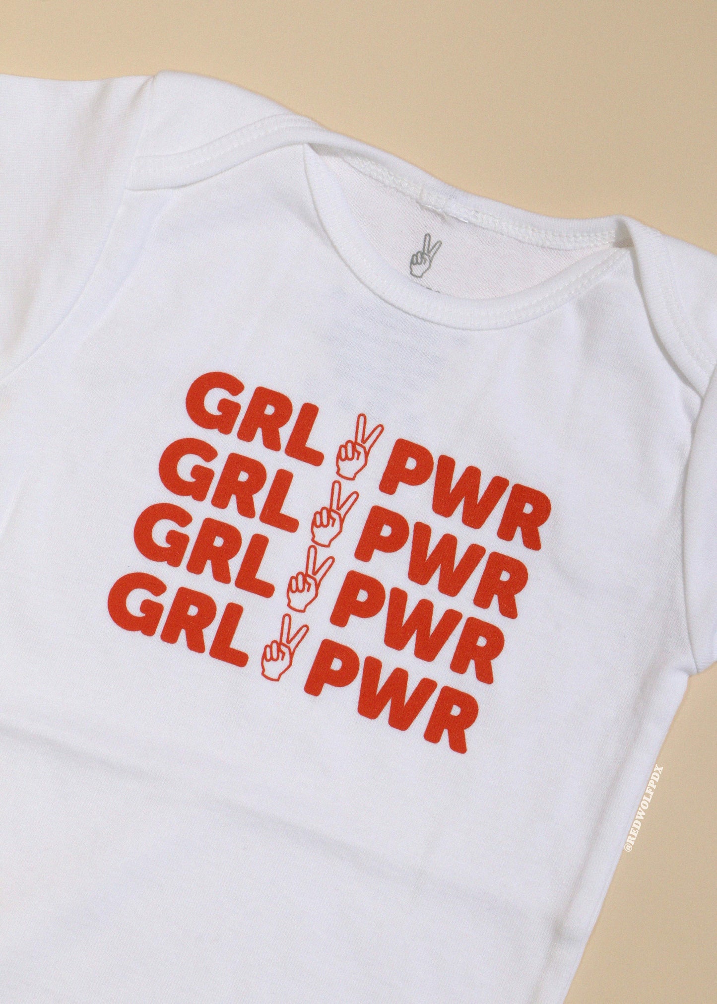 baby onesie with red 'GRL PWR' text and peace signs on a beige background
