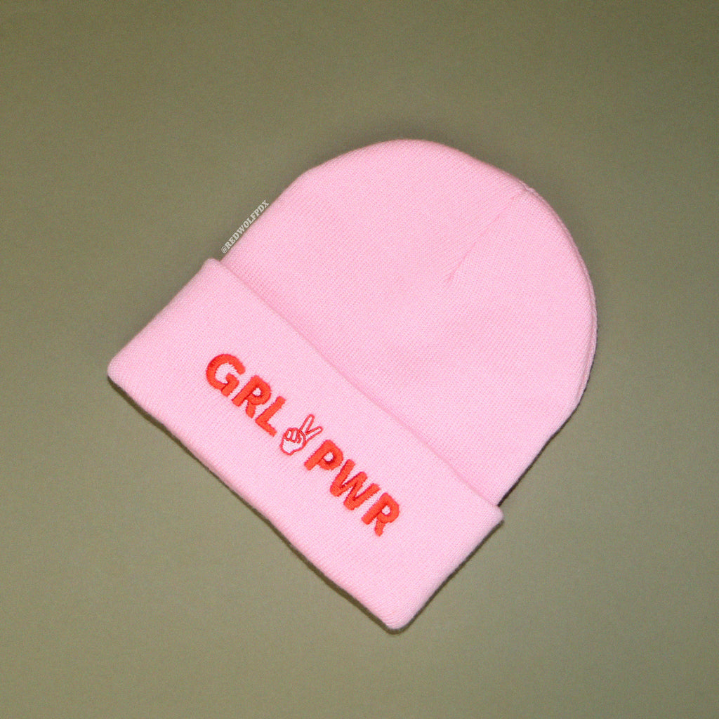 light pink beanie with text 'GRL PWR' in red thread embroidered across band of the beanie against a vintage green background.