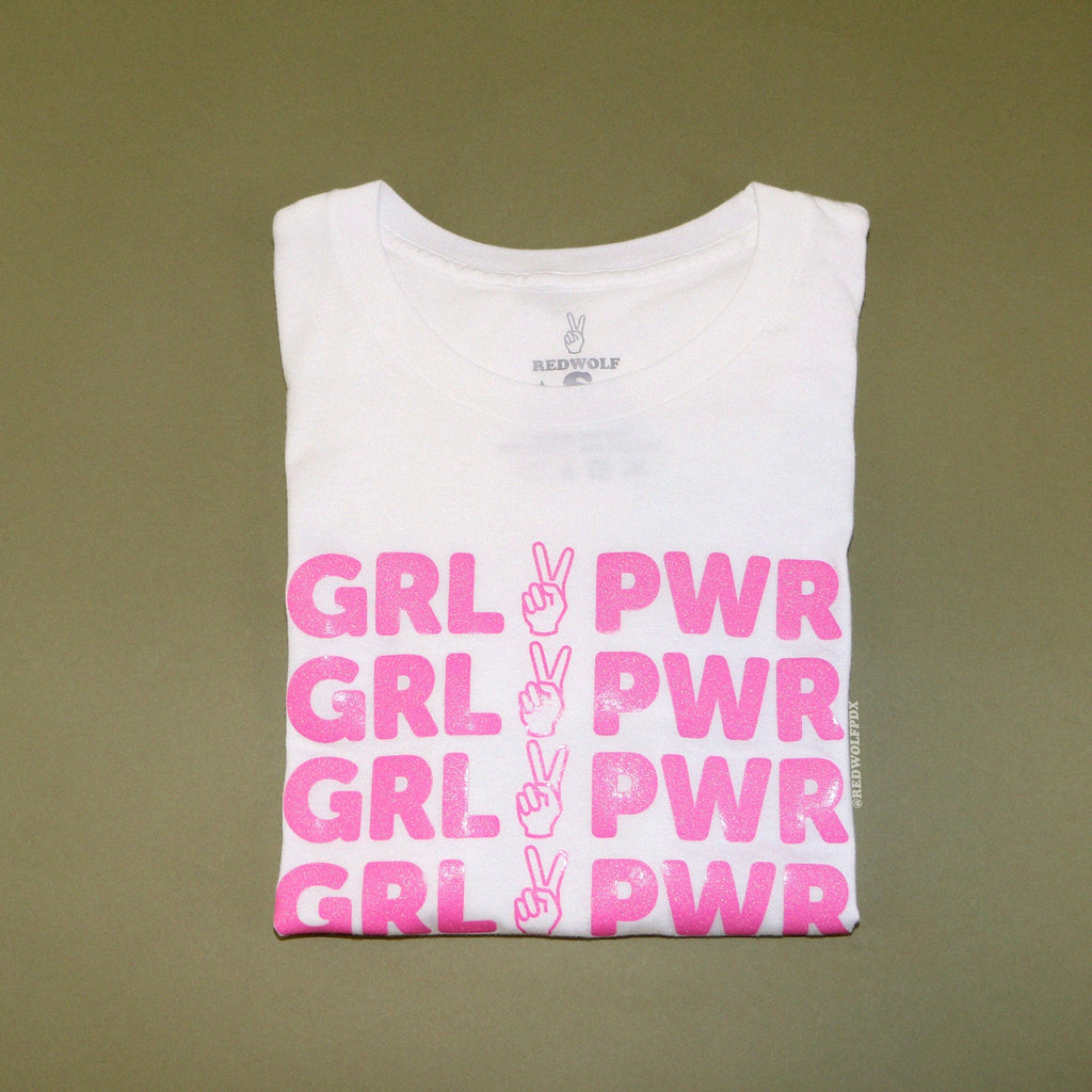 folded white graphic tee with text 'GRL PWR' in pink glitter vinyl screen printed