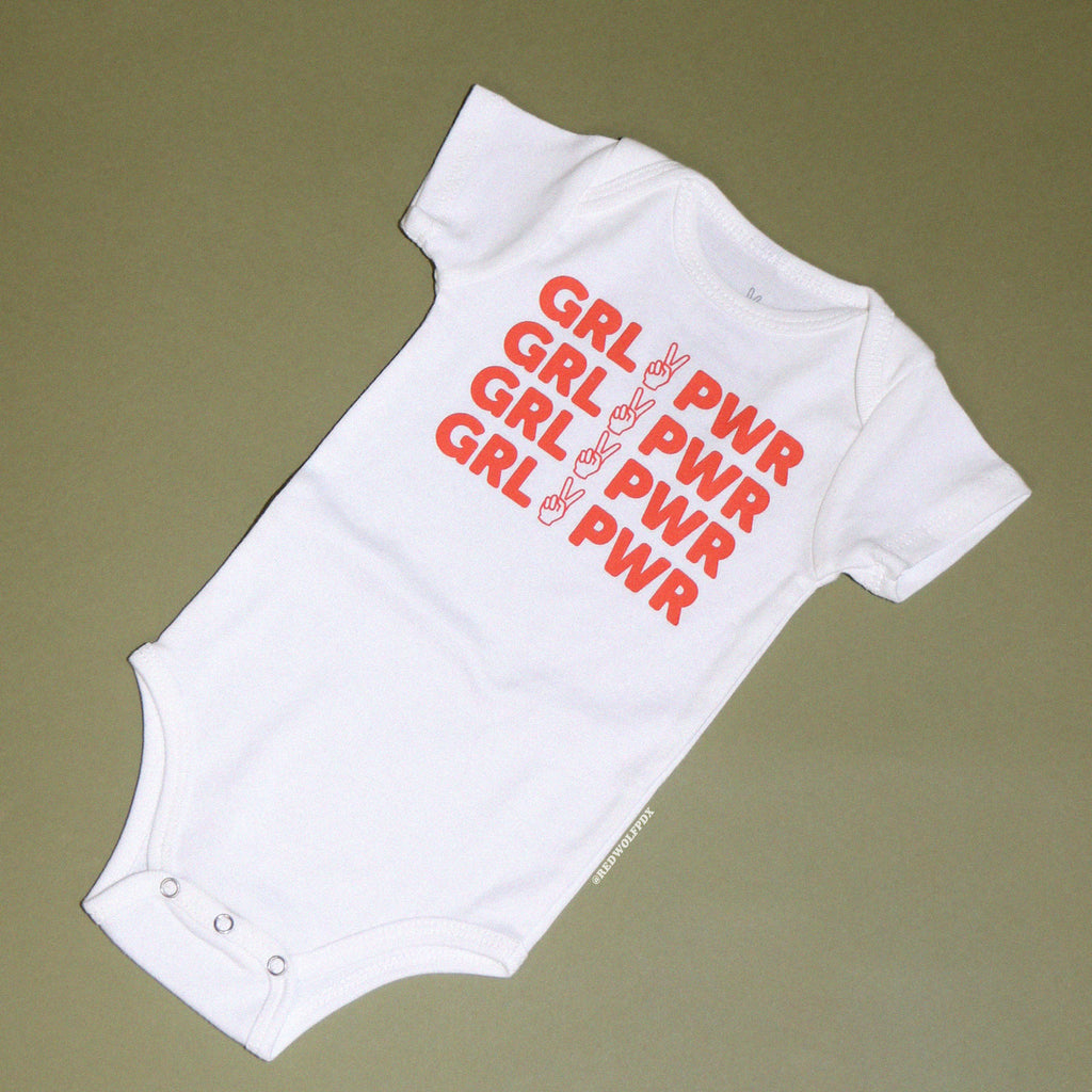 white onesie for babies with text 'GRL PWR' in orange red ink screen printed on front on a vintage green background