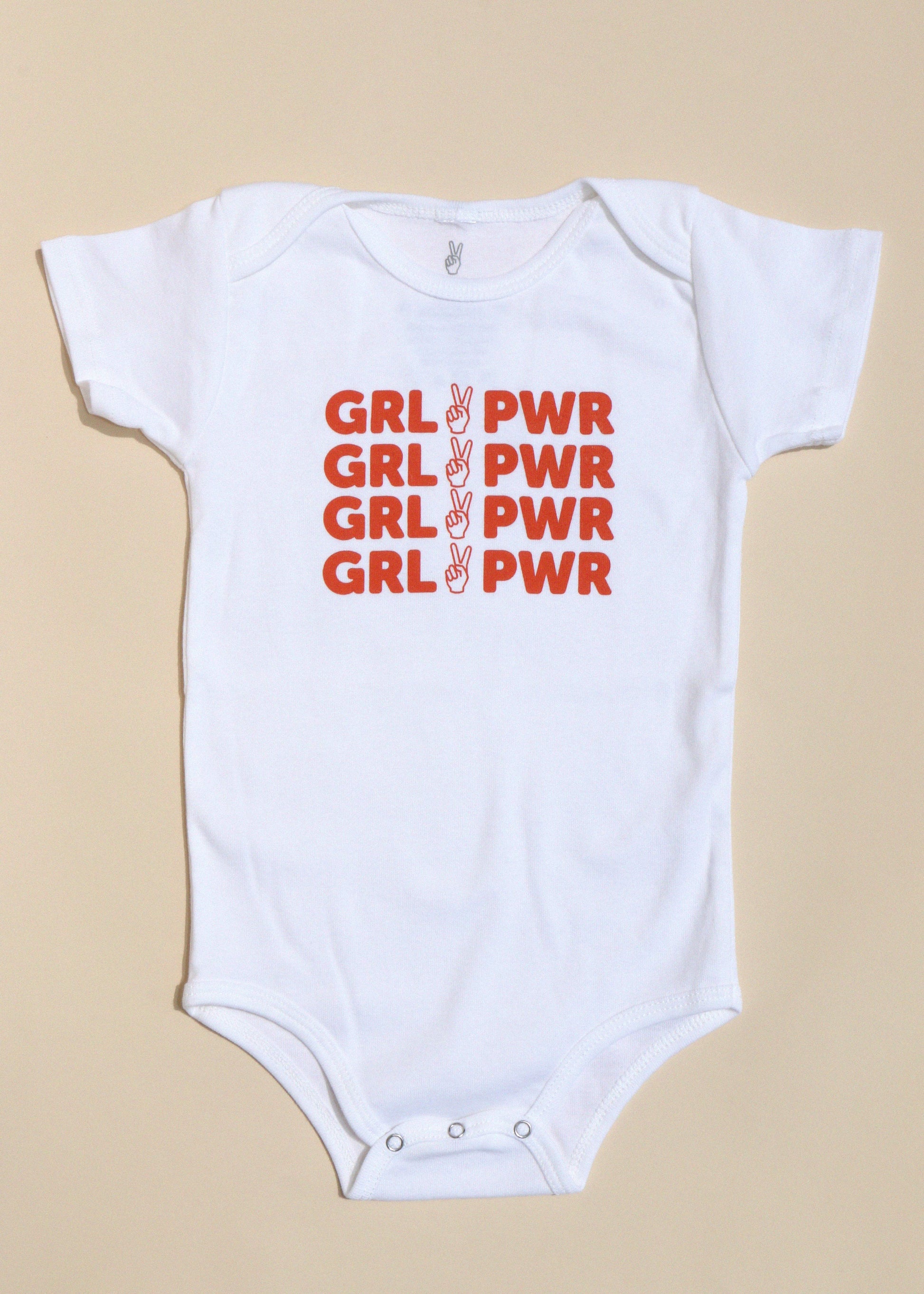 White baby onesie with red 'GRL PWR' text on a beige background