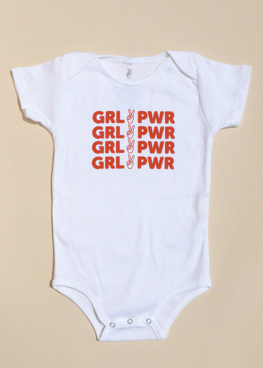 White baby onesie with red 'GRL PWR' text on a beige background